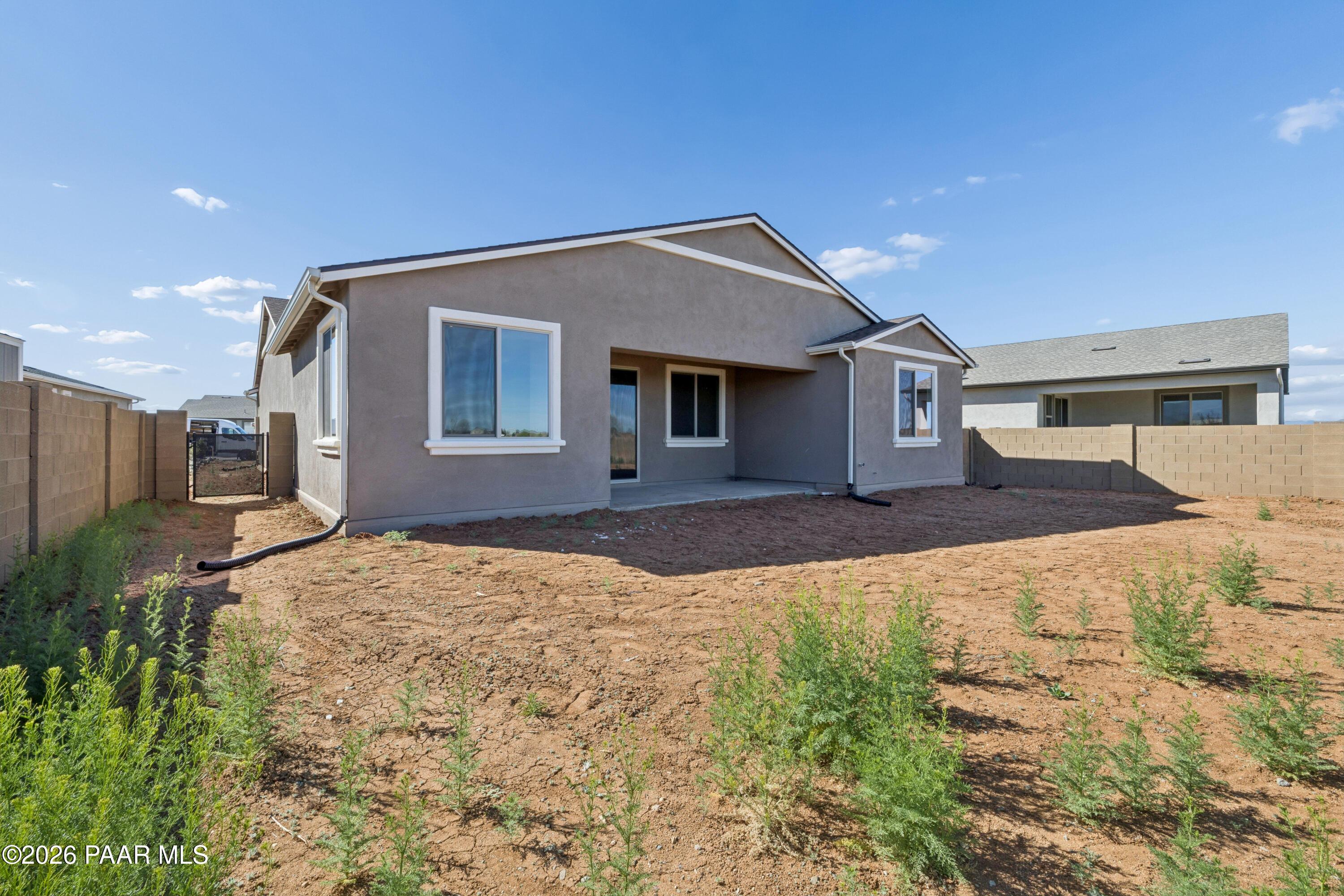 Tan stucco single-story home exterior with covered patio, sliding doors, and fenced dirt backyard in North Ridge at Pronghorn Ranch, Prescott Valley, Arizona
