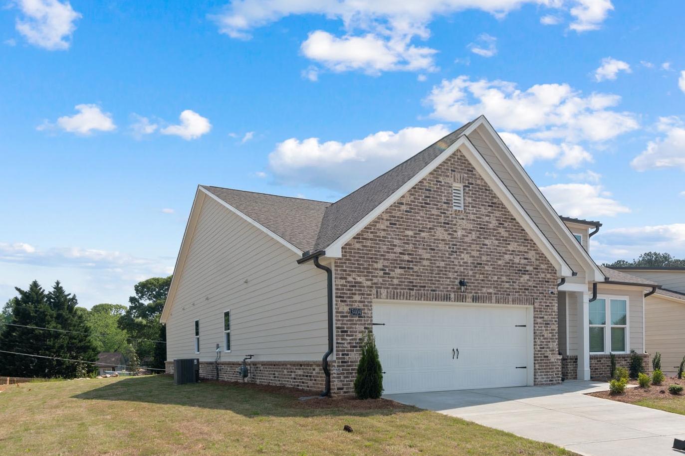 Side elevation of The Glenwood C single-story home in Hoschton, GA, with brick accents, beige siding, and 2-car garage