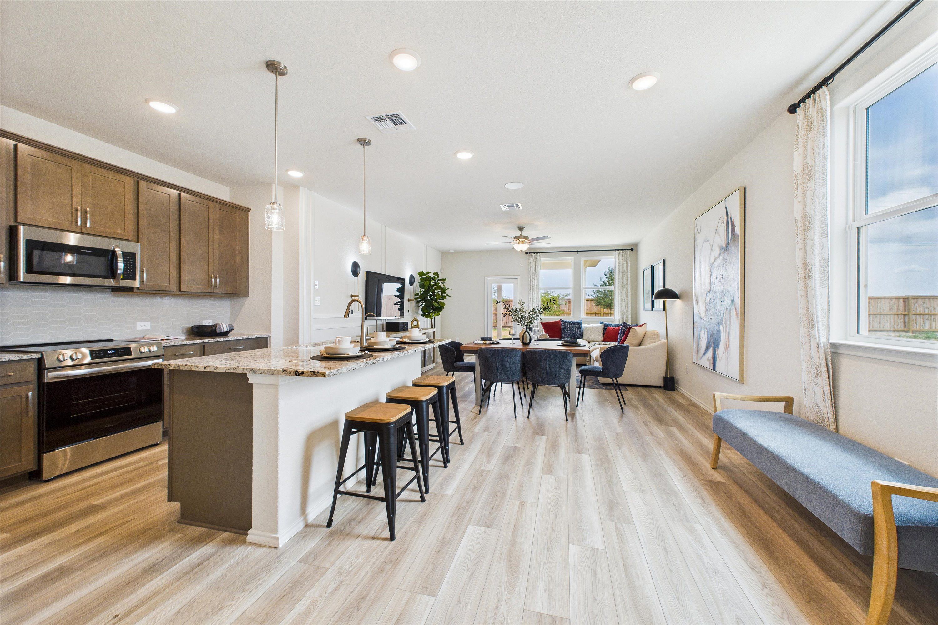 Modern open-concept kitchen and dining in Agave San Antonio TX home with wood floors, quartz island, bar stools, and large windows