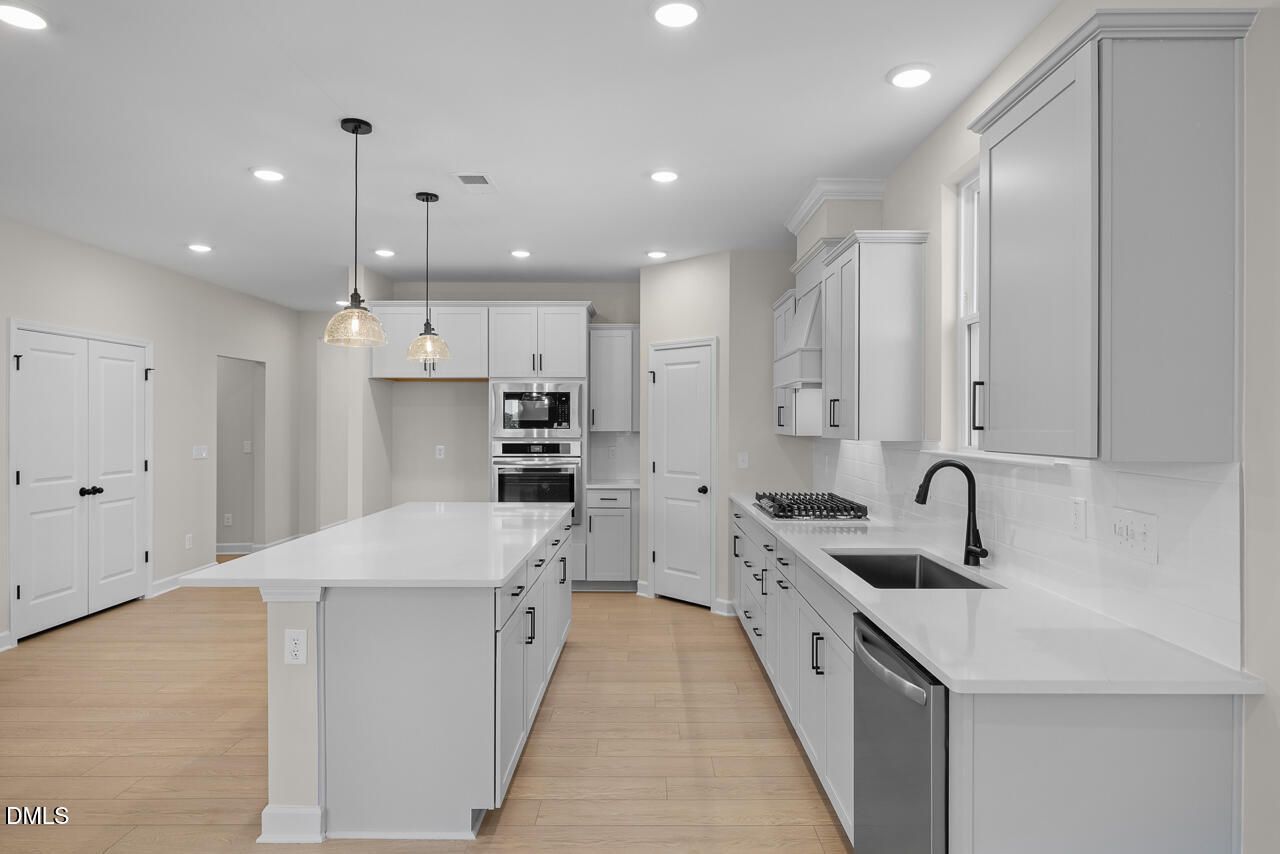 Modern kitchen with white shaker cabinets, large island, quartz countertops, and stainless appliances in Davidson Homes Ashport M plan, Wendell Ridge
