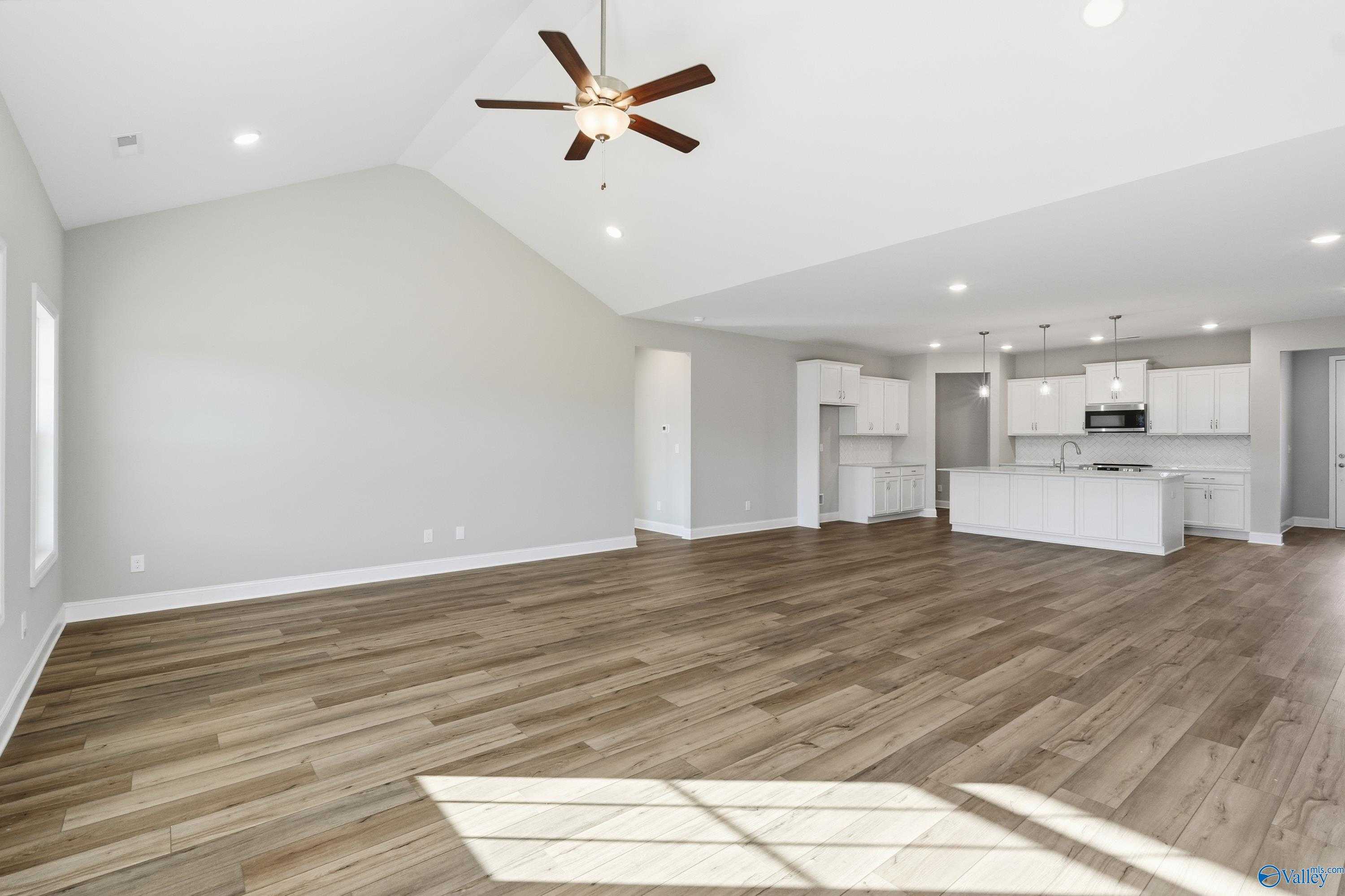Open-concept kitchen and living space with vaulted ceiling, hardwood floors, and white cabinetry in The Lanier 4-bedroom home, Toney, Alabama