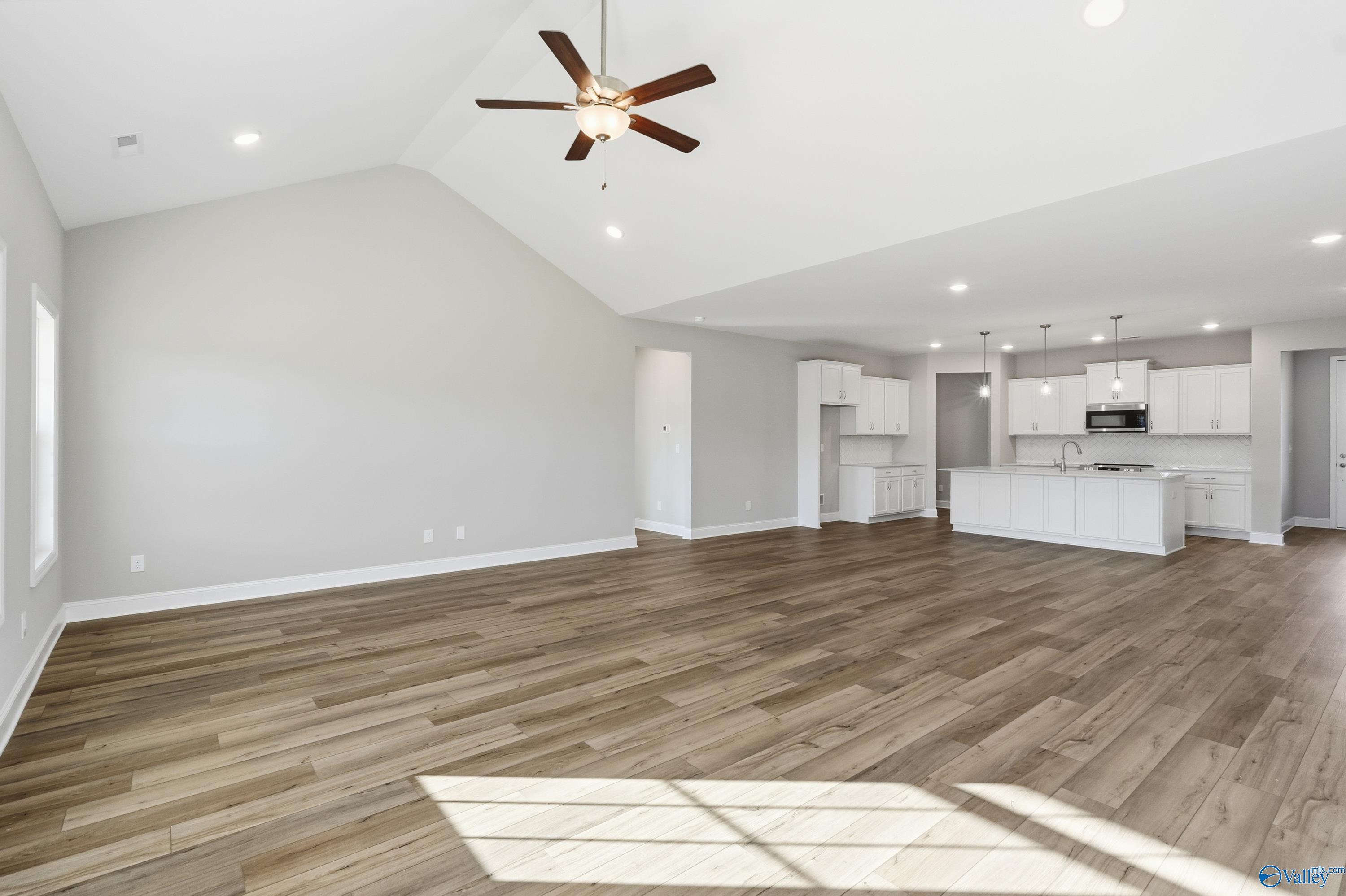 Open-concept living and kitchen area with vaulted ceiling, fan, white cabinets, hardwood floors in Davidson Homes The Lanier, Toney, Alabama