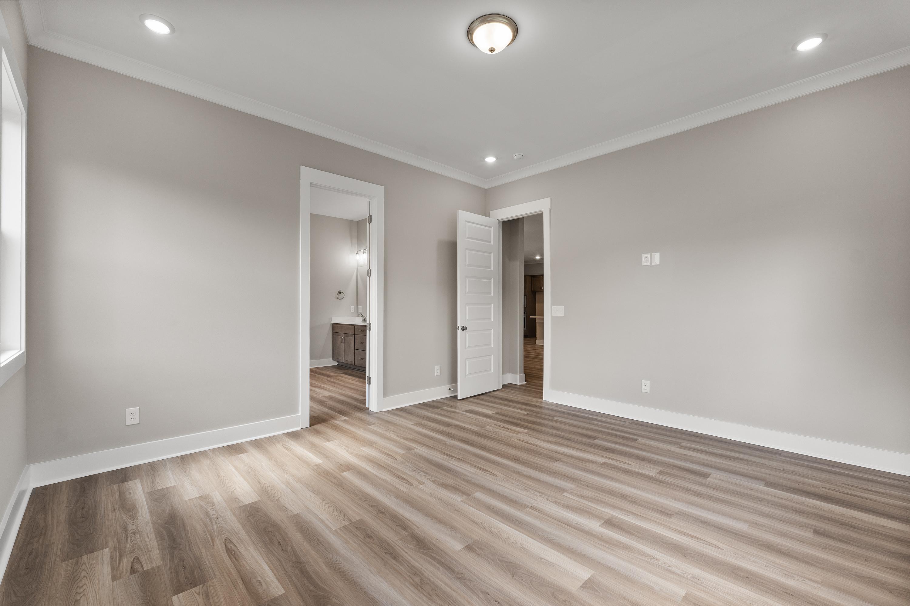 Spacious master bedroom in The Oxford C with light gray walls, hardwood floors, and ensuite bath door
