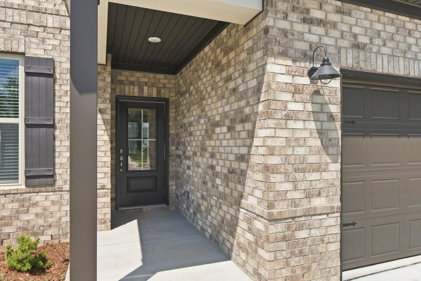 Covered front porch with brick exterior and black front door at Davidson Homes The Willow C in Woods Crossing, Gallatin, TN