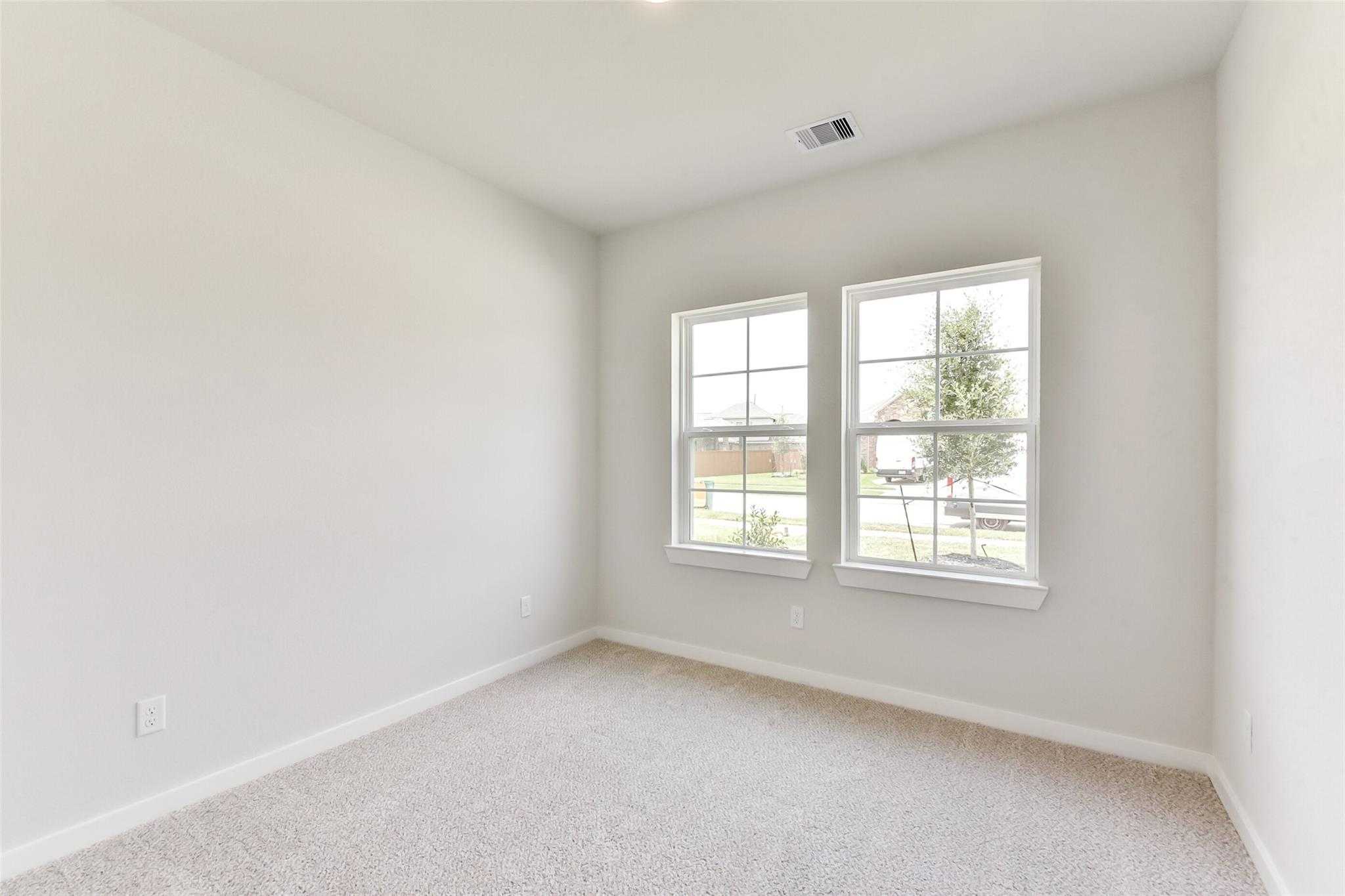 Bright secondary bedroom with large windows, beige carpet, and natural light in Davidson Homes The Laguna C, Rosharon, Texas