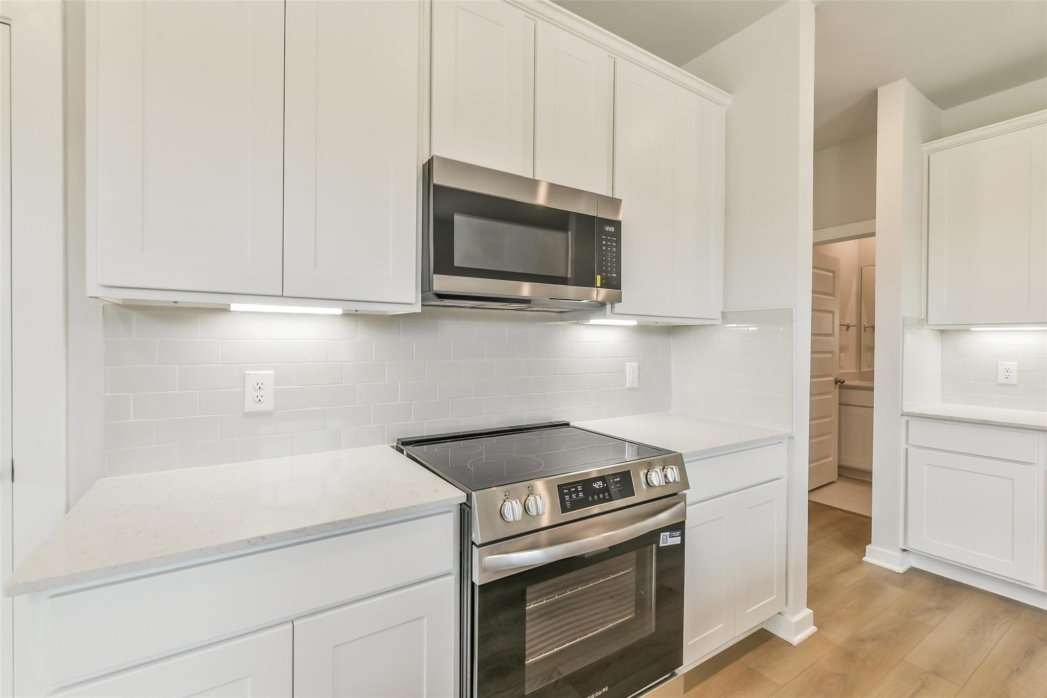 Modern white shaker kitchen with subway tile backsplash, quartz counters, stainless steel range in The Frio G, Conroe, Texas