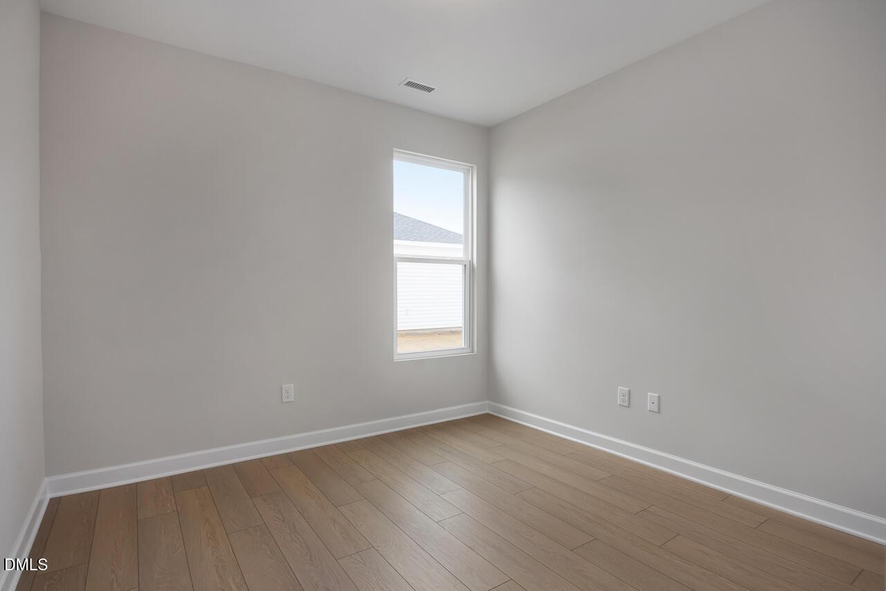 Bright secondary bedroom with light gray walls, large window, and hardwood floors in The Daphne C by Davidson Homes, Lillington, NC