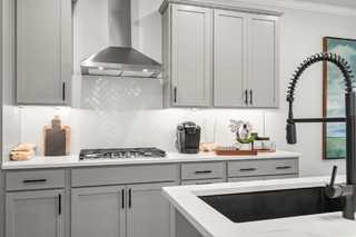 Modern kitchen in The Washington H townhome with gray shaker cabinets, stainless steel hood, subway tile backsplash, and black faucet