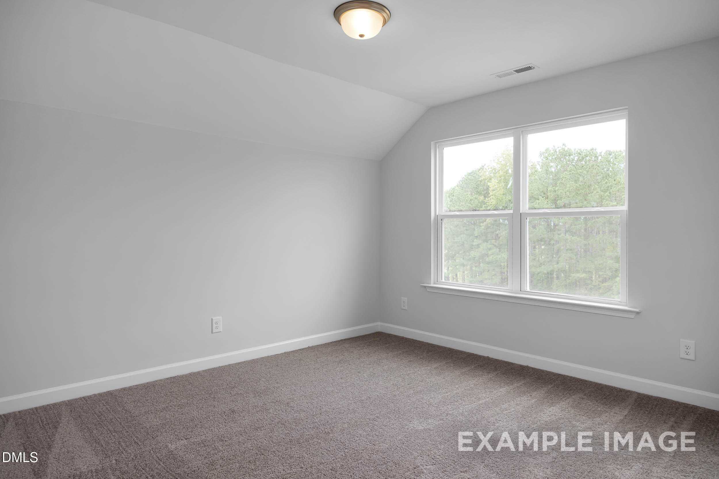 Spacious upstairs bedroom with vaulted ceiling, large windows overlooking trees, gray walls, and carpet in Davidson Homes The Ash B, Lillington, NC