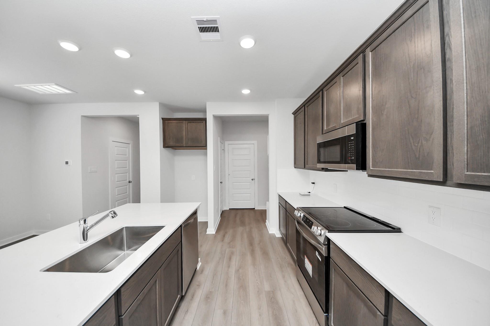 Modern kitchen with dark wood cabinets and white countertops in The Brazos F floor plan at Liberty Estates, Cleveland, TX.
