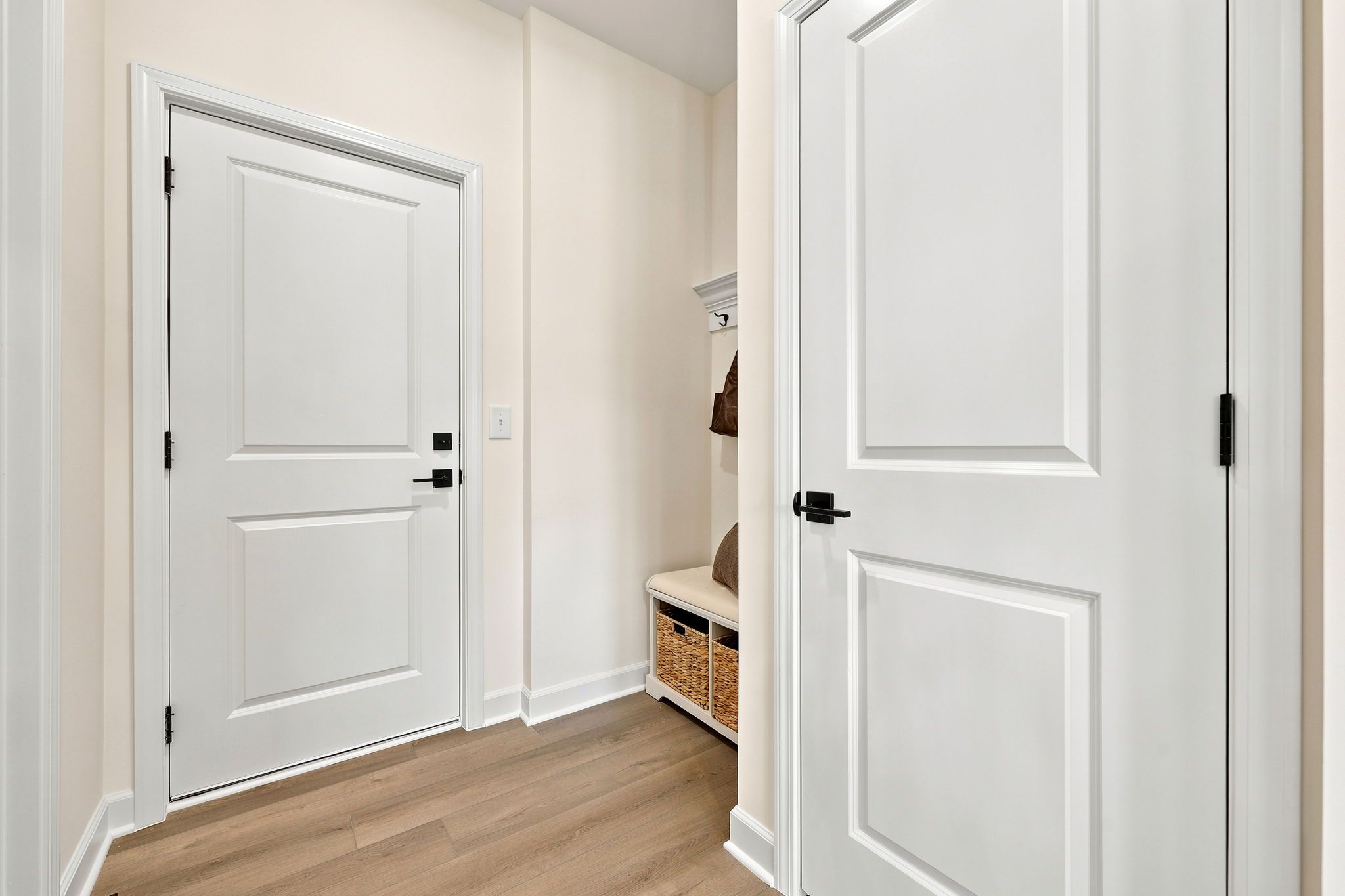 Mudroom entry in The Beech B featuring white doors, matte black hardware, and a built-in storage bench with baskets.