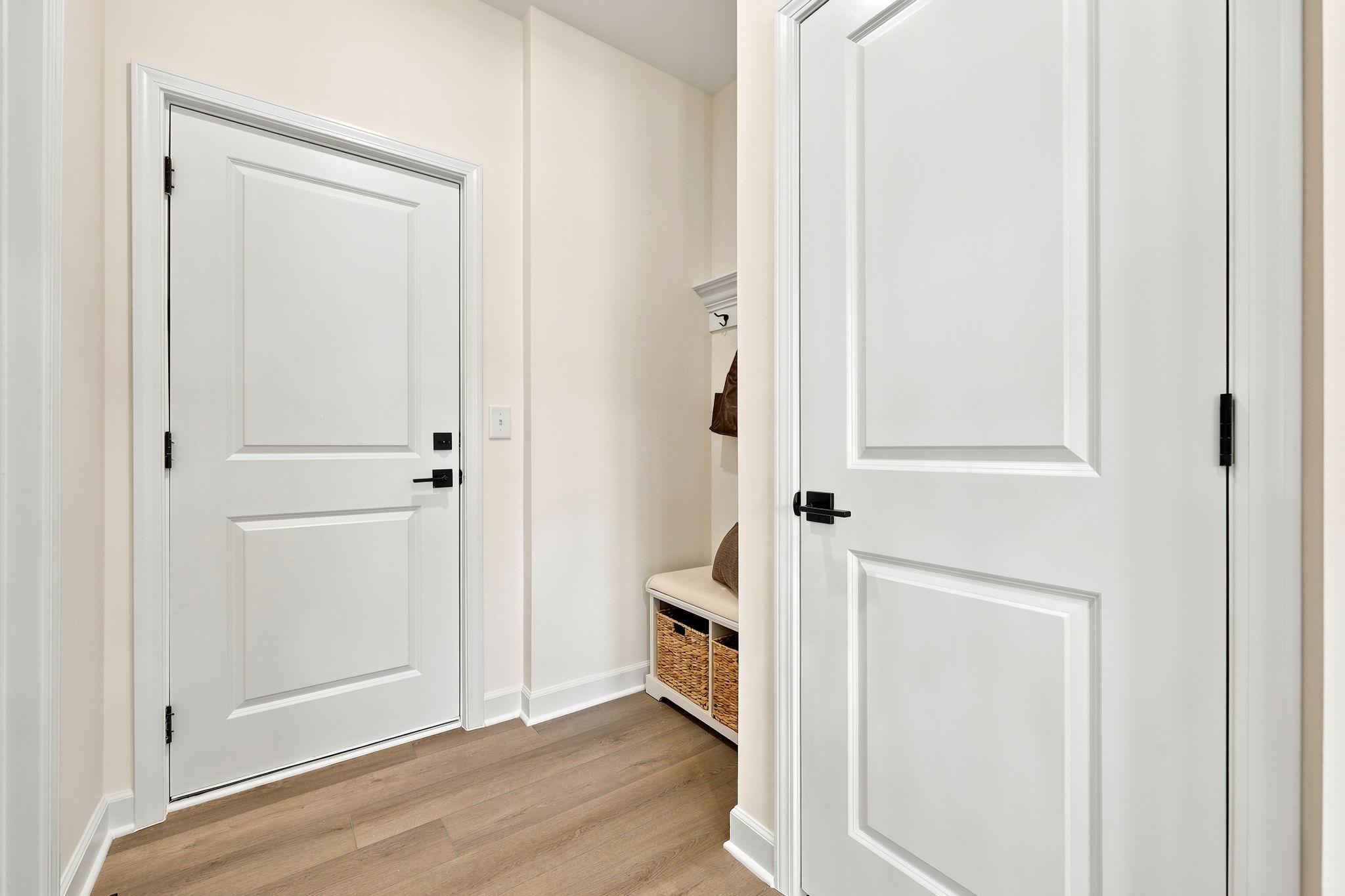 Mudroom entry in The Beech B featuring white doors, matte black hardware, and a built-in storage bench with baskets.