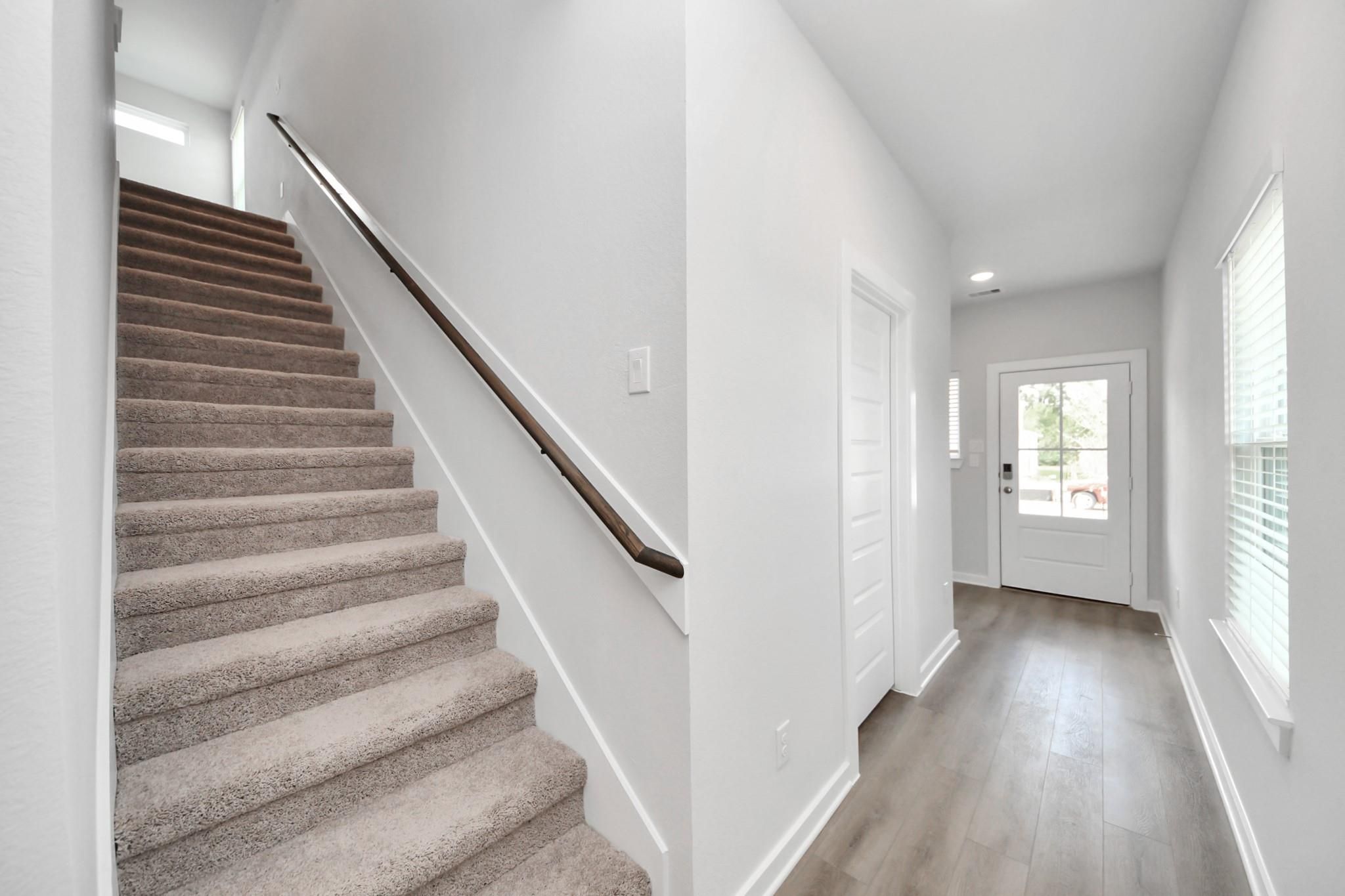 Bright entryway with carpeted staircase, wood handrail, and glass-paneled front door in The Sabine F, Caney Creek Place, Conroe, Texas