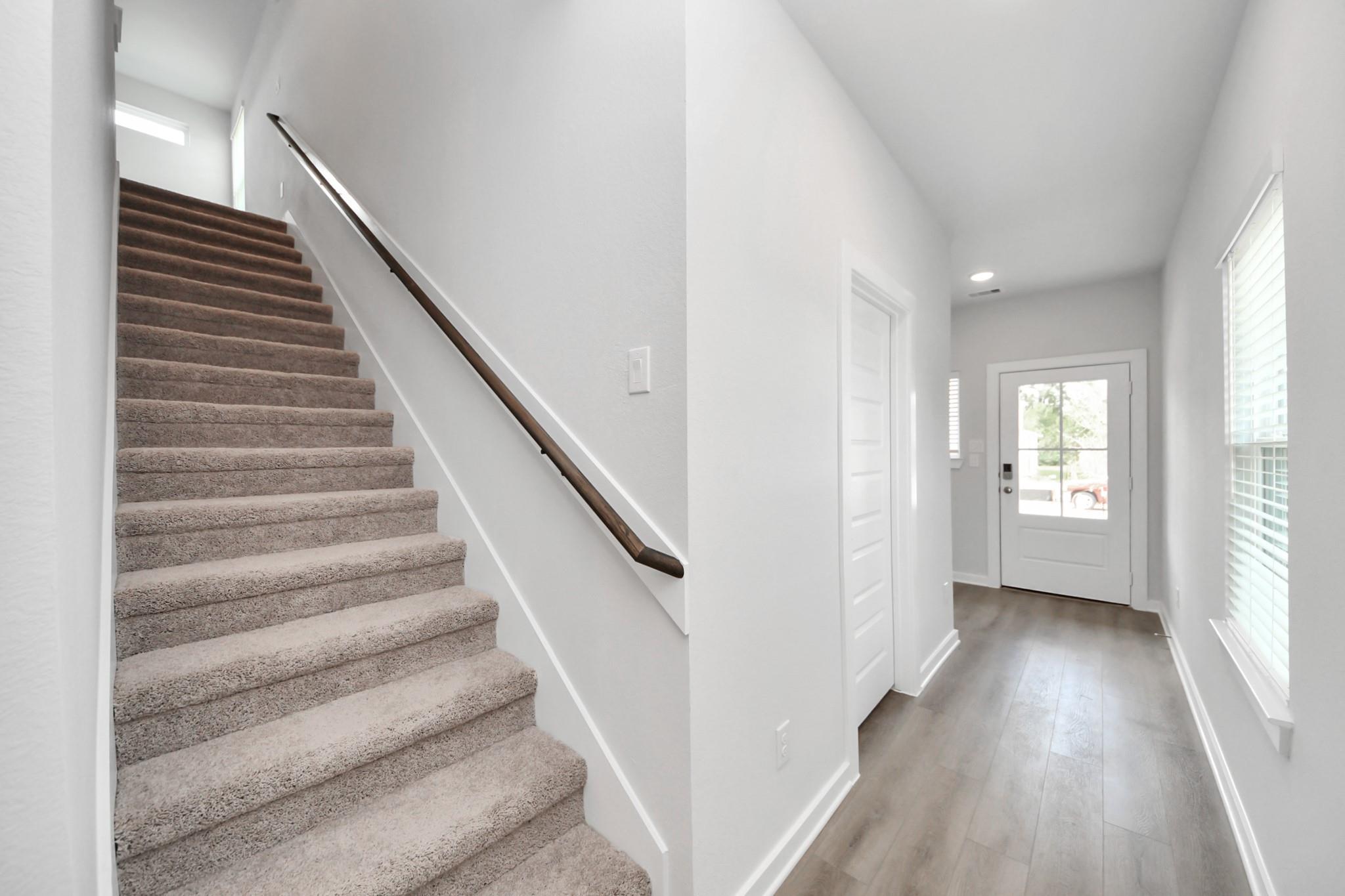 Bright entryway with carpeted staircase, wood handrail, and glass-paneled front door in The Sabine F, Caney Creek Place, Conroe, Texas