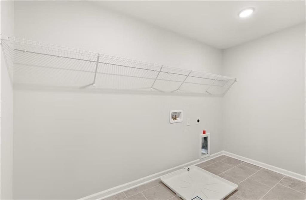 Spacious laundry room with wire shelving, washer-dryer hookups, pet door, and tiled floor in Davidson Homes The Hickory B, Winder, Georgia