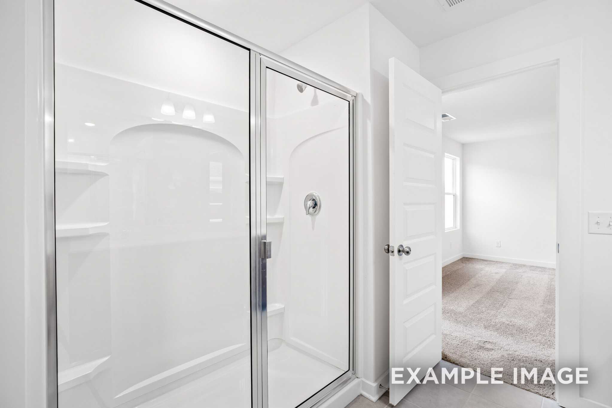 Spacious master bath in The Grayson C featuring frameless glass shower with arched niche and open bedroom door