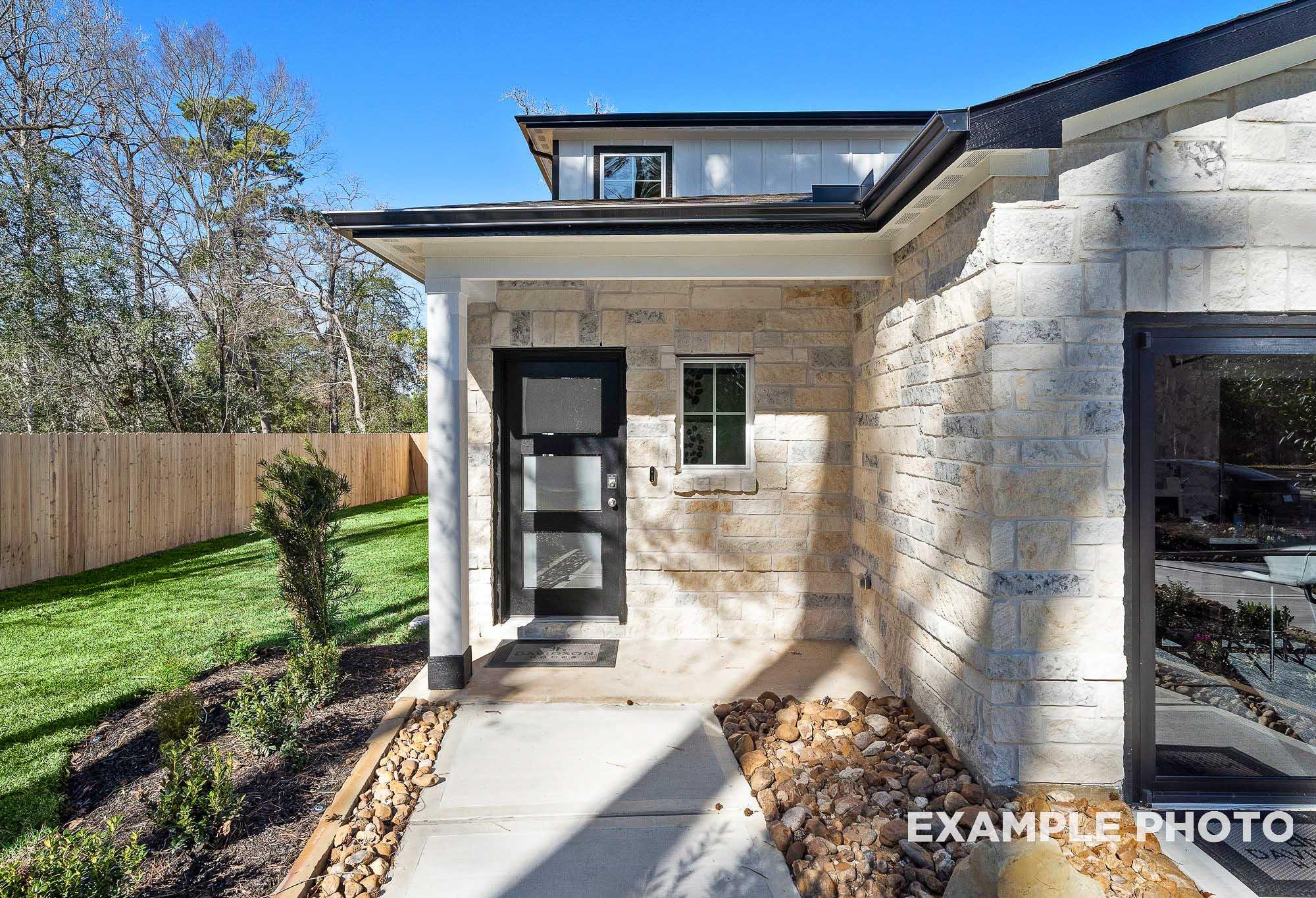 Modern stone exterior of The San Marcos two-story home with black glass door, columned porch, and lush landscaping