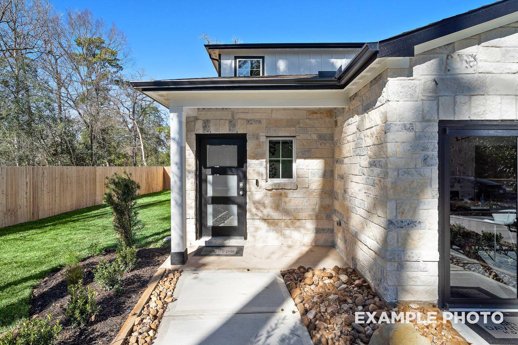 Modern stone exterior of The San Marcos two-story home with black glass door, columned porch, and lush landscaping