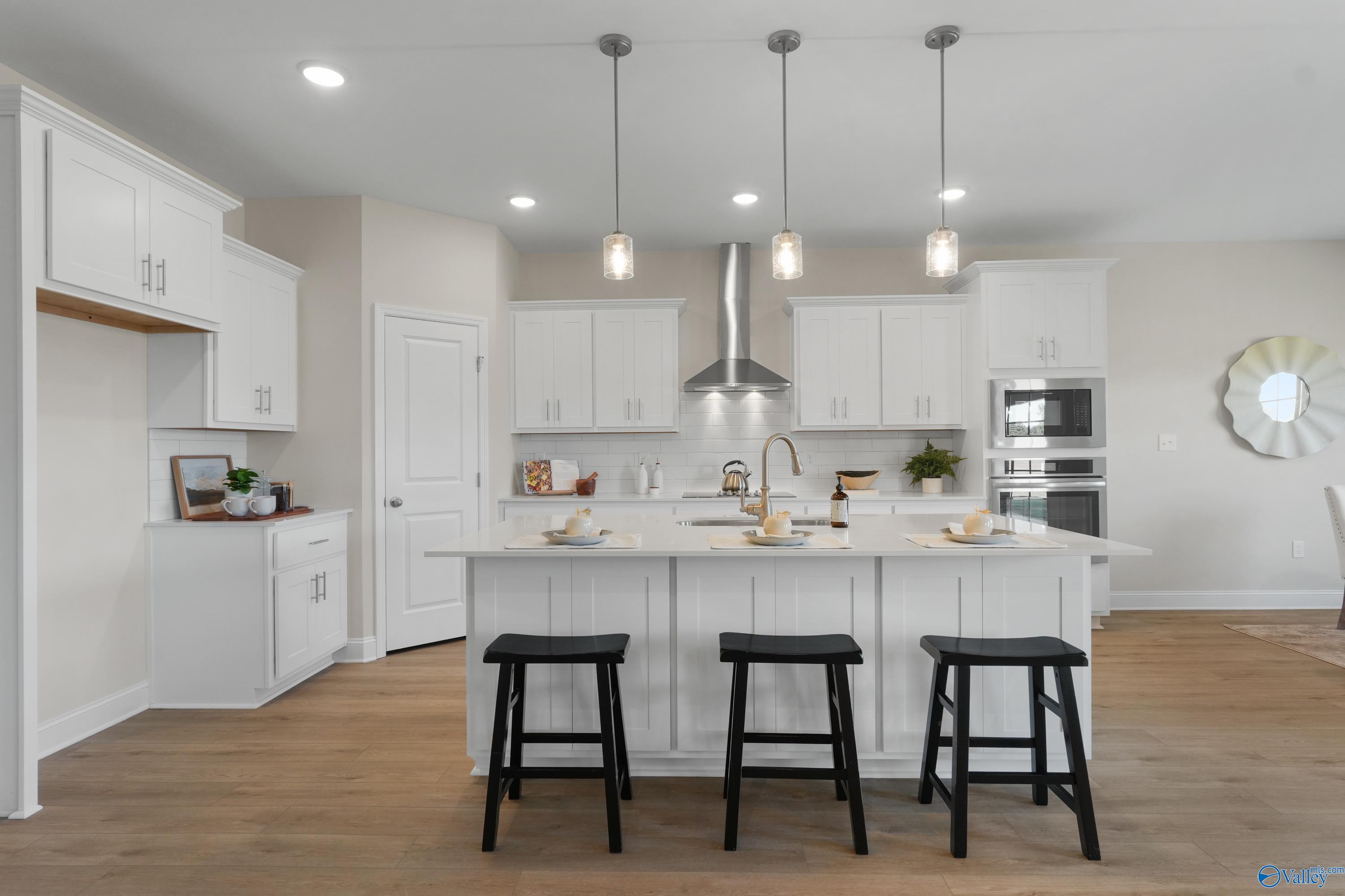 Spacious modern kitchen with white cabinets, large island, black bar stools, and stainless appliances in Davidson Homes The Rockford B, Toney, Alabama