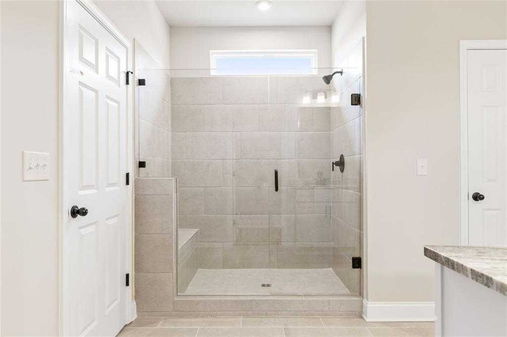 Modern frameless glass shower with beige tile, built-in bench, and rainfall head in master bath of Davidson Homes The Harrison G, Hoschton, GA