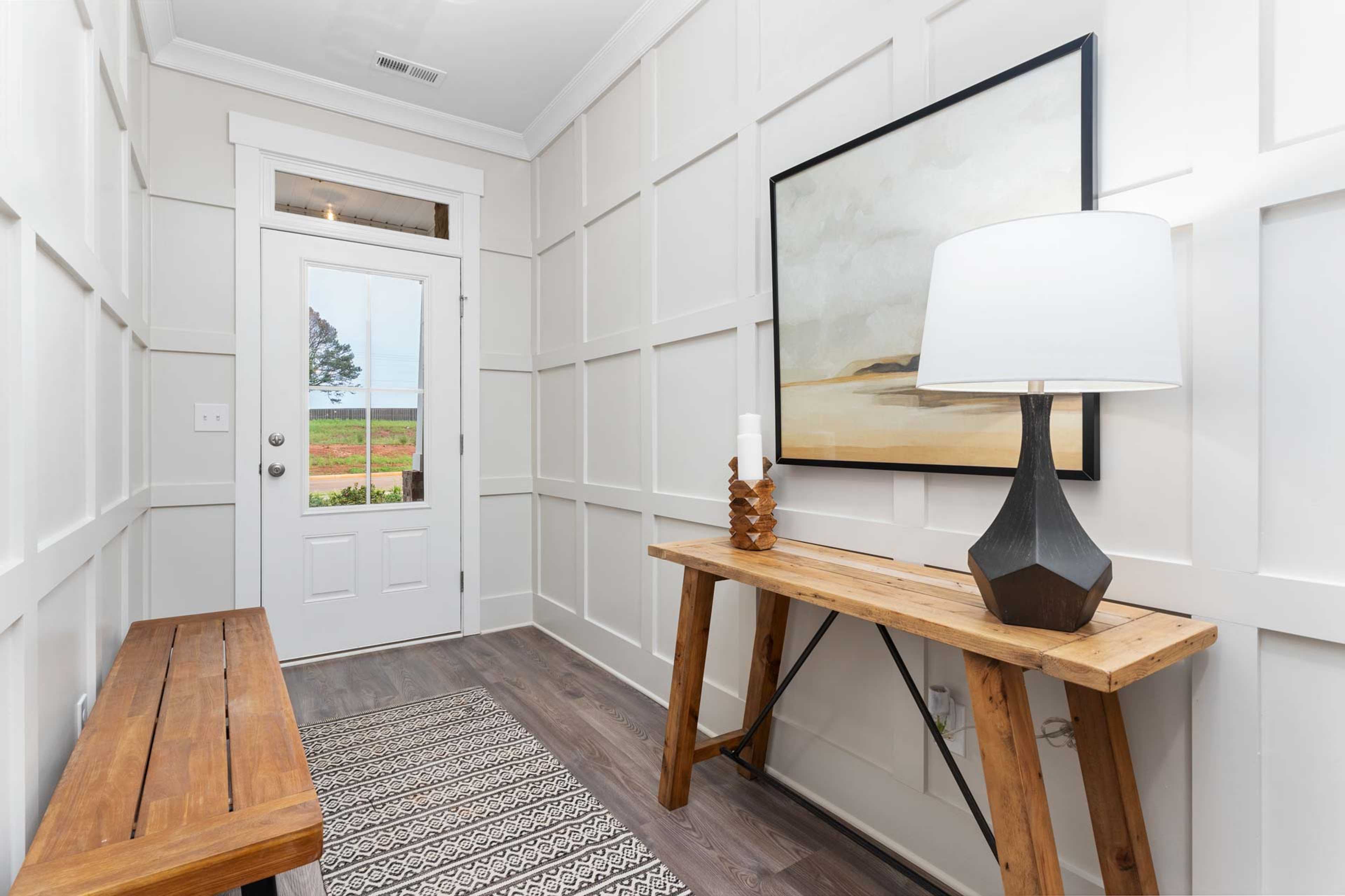 Cozy entryway at The Meadows in Athens Alabama with white shiplap walls, wooden console table, lamp, bench and rural field view