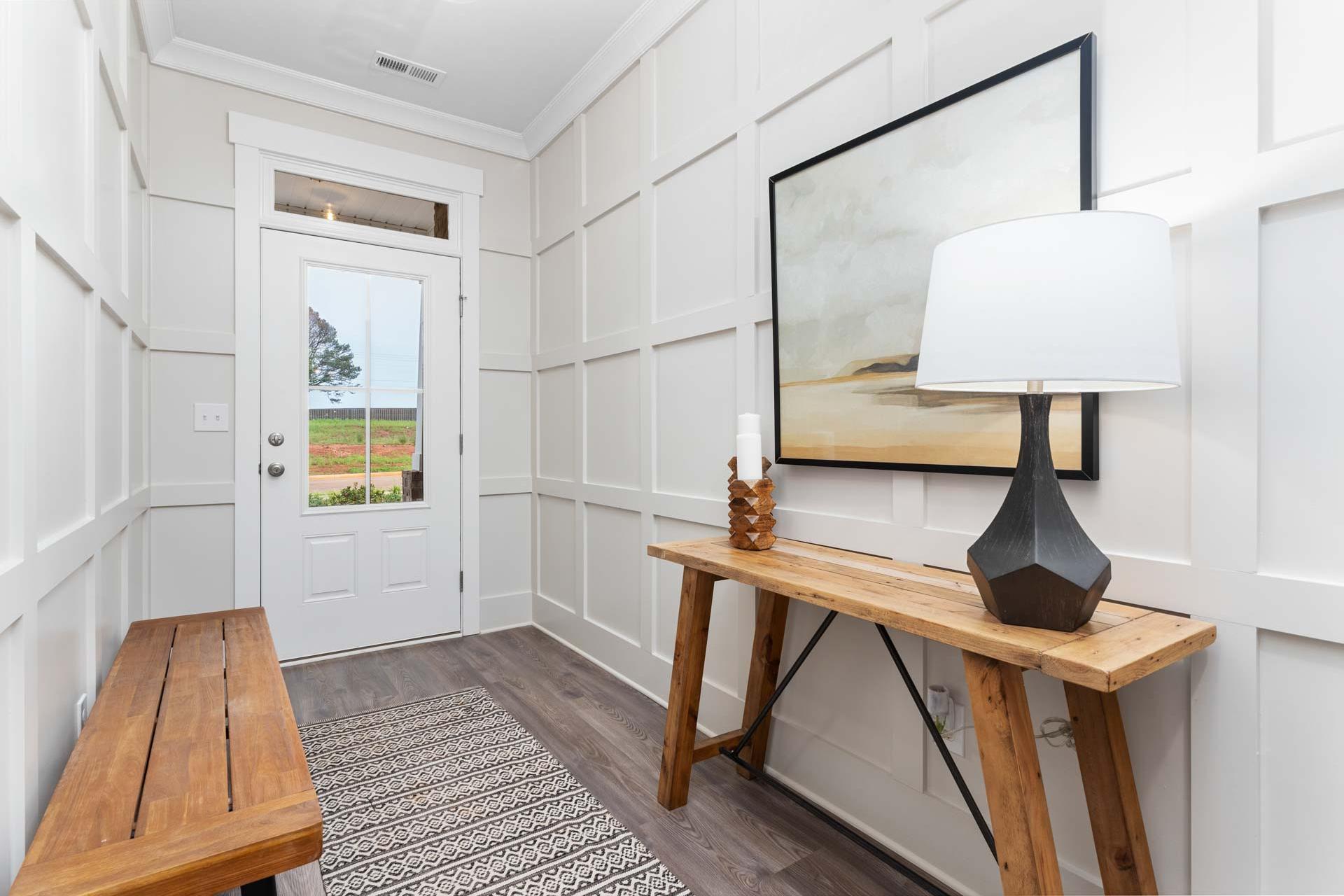 Cozy entryway at The Meadows in Athens Alabama with white shiplap walls, wooden console table, lamp, bench and rural field view
