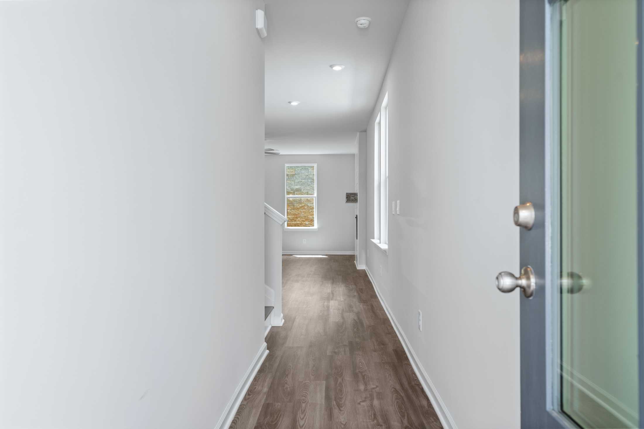 Spacious hallway in The Cary A 2-story home featuring light wood floors, white walls, ascending staircase, and window to upper master suite