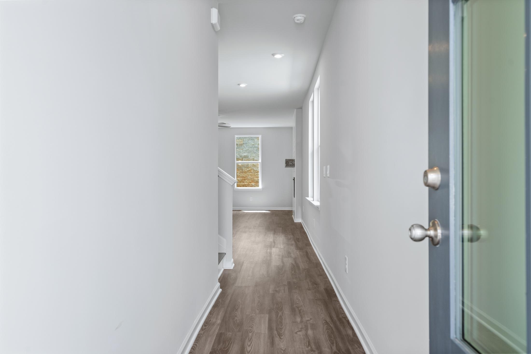 Spacious hallway in The Cary A 2-story home featuring light wood floors, white walls, ascending staircase, and window to upper master suite