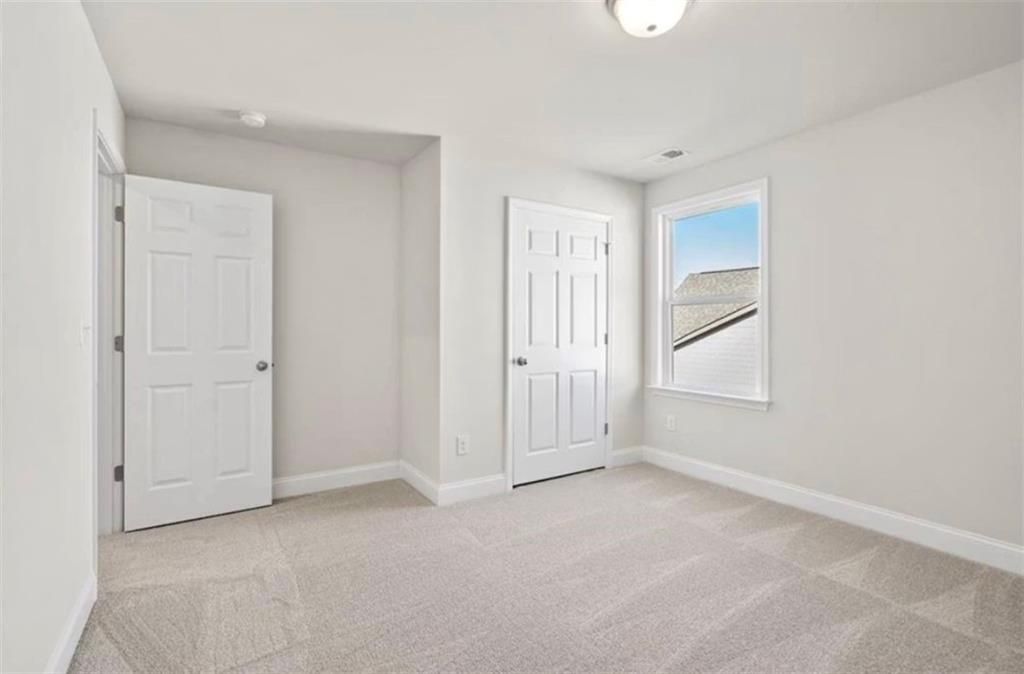 Bright, carpeted bedroom with white walls and natural light in The Ash C floor plan at Wehunt Meadows, Hoschton, Georgia.