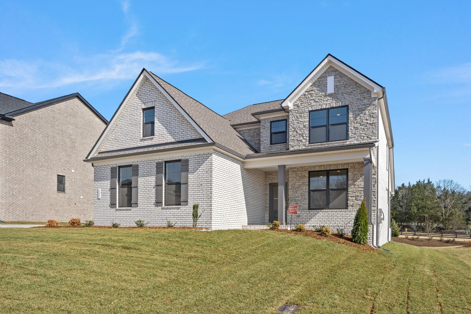 Two-story beige brick home with gabled roof, covered porch, dark shutters, and green lawn in Benders Cove, Mt. Juliet