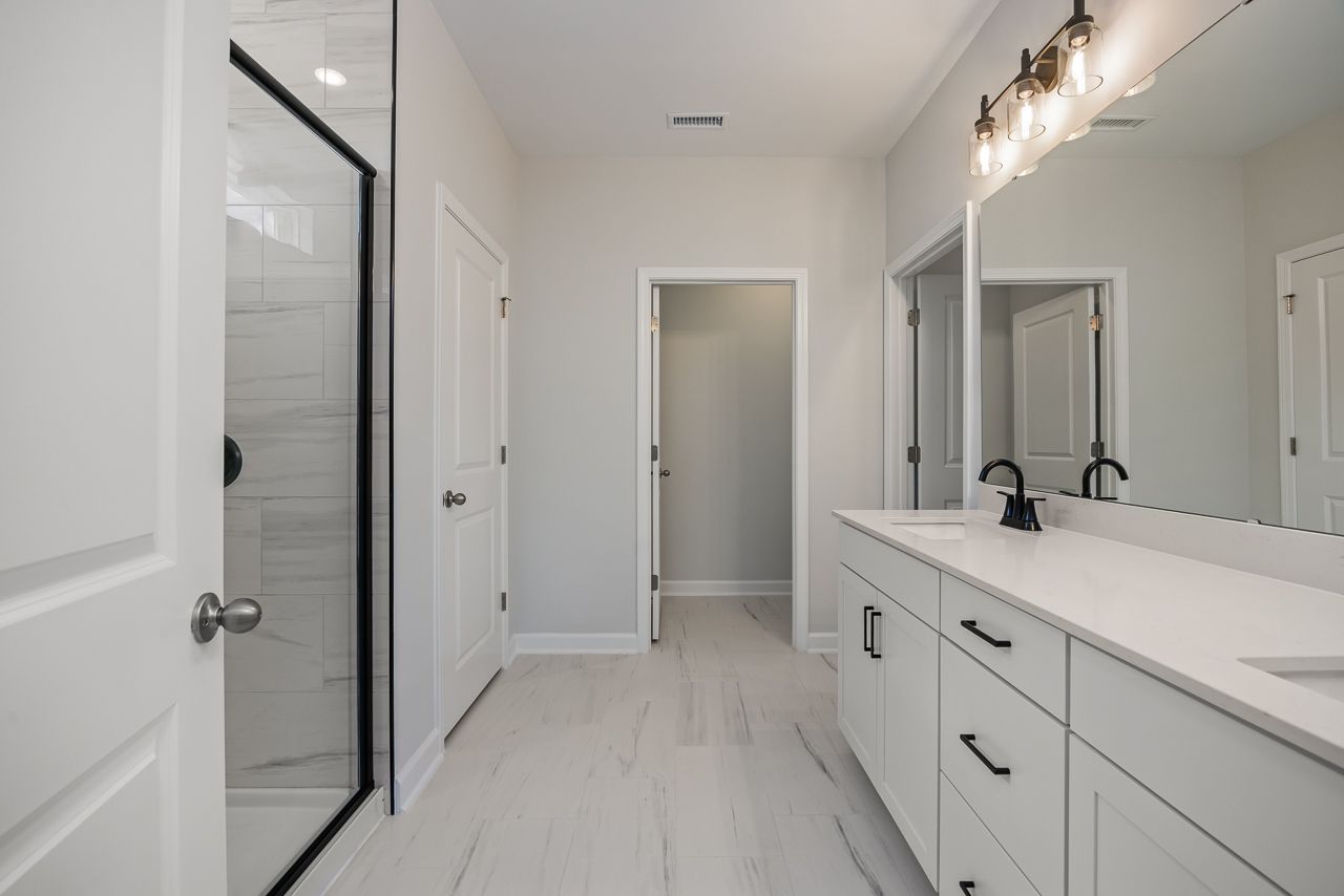 Modern primary bathroom in The Birch II featuring a dual-sink vanity, tiled walk-in shower, and sleek finishes.