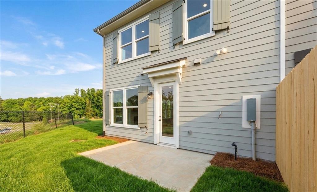 Modern two-story gray-sided home with glass French door, concrete patio, lush green lawn, wooden fence, and trees in Hemingway, Cumming, Georgia - Davidson Homes The Durham B