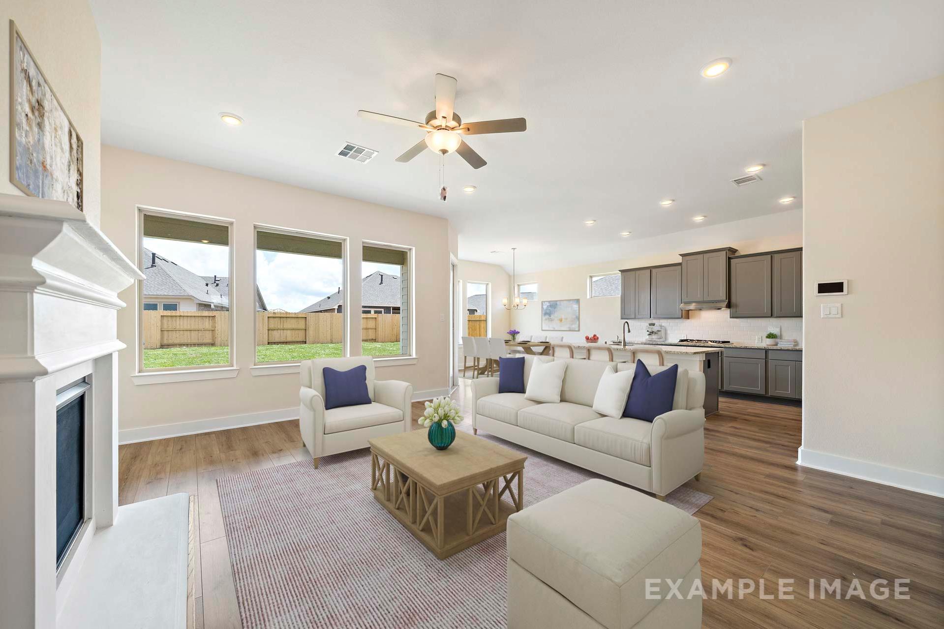 Spacious open-concept living room in The Diana C Davidson Homes with white fireplace, beige sectional sofa, ceiling fan, and kitchen views