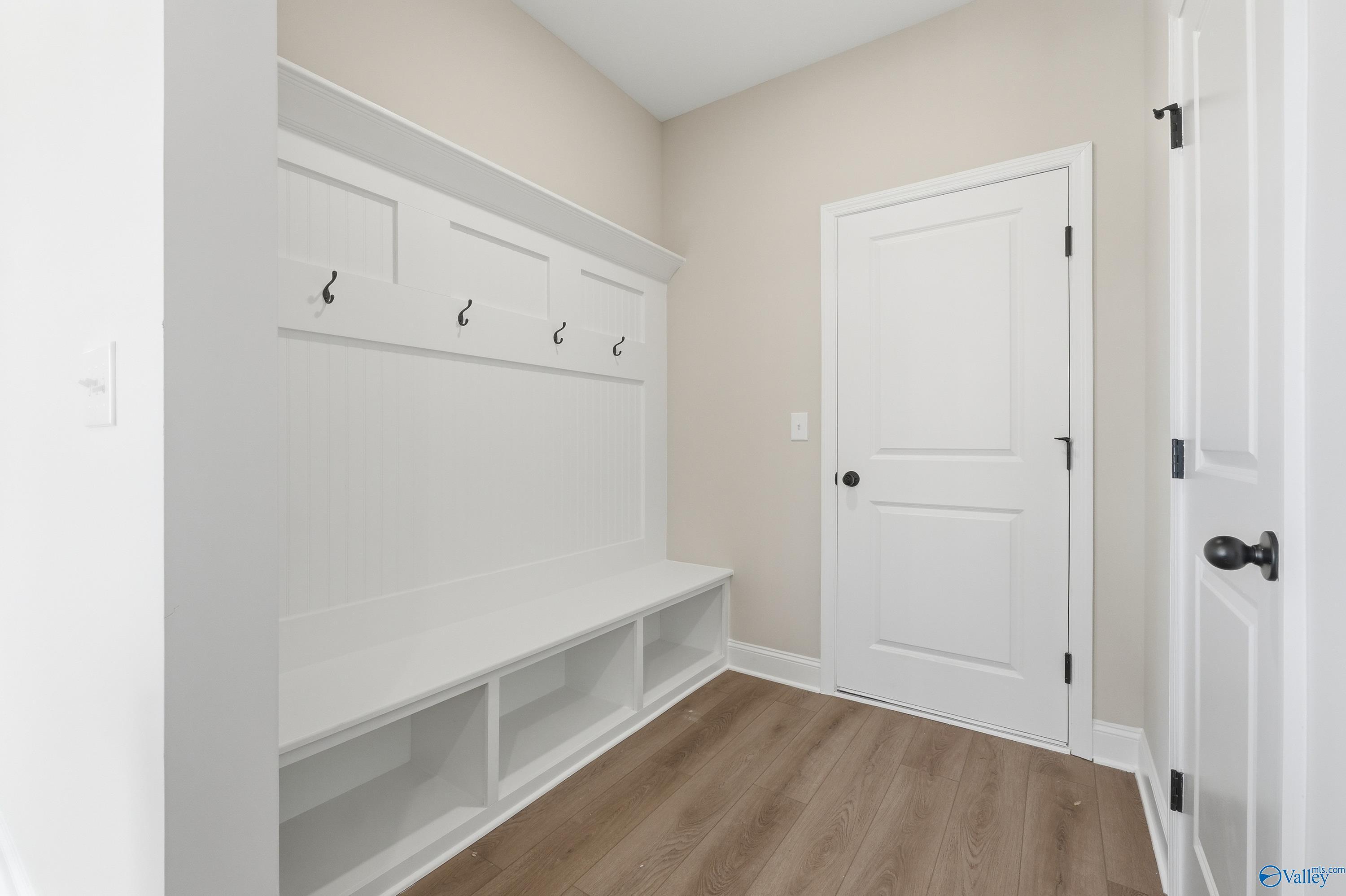 Functional mudroom with white built-in cabinets, coat hooks, bench, and hardwood floors in Davidson Homes Chelsea D, Noble Ridge, Cullman