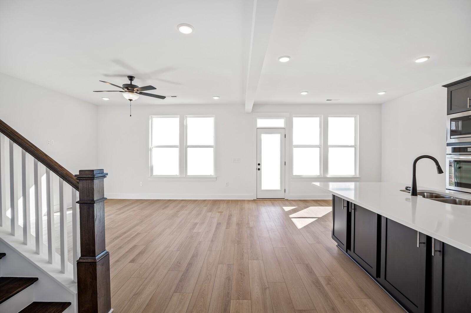 Open living area with hardwood floors, wooden staircase, large windows, and modern kitchen featuring dark cabinets in Davidson Homes The Willow C, Gallatin, TN