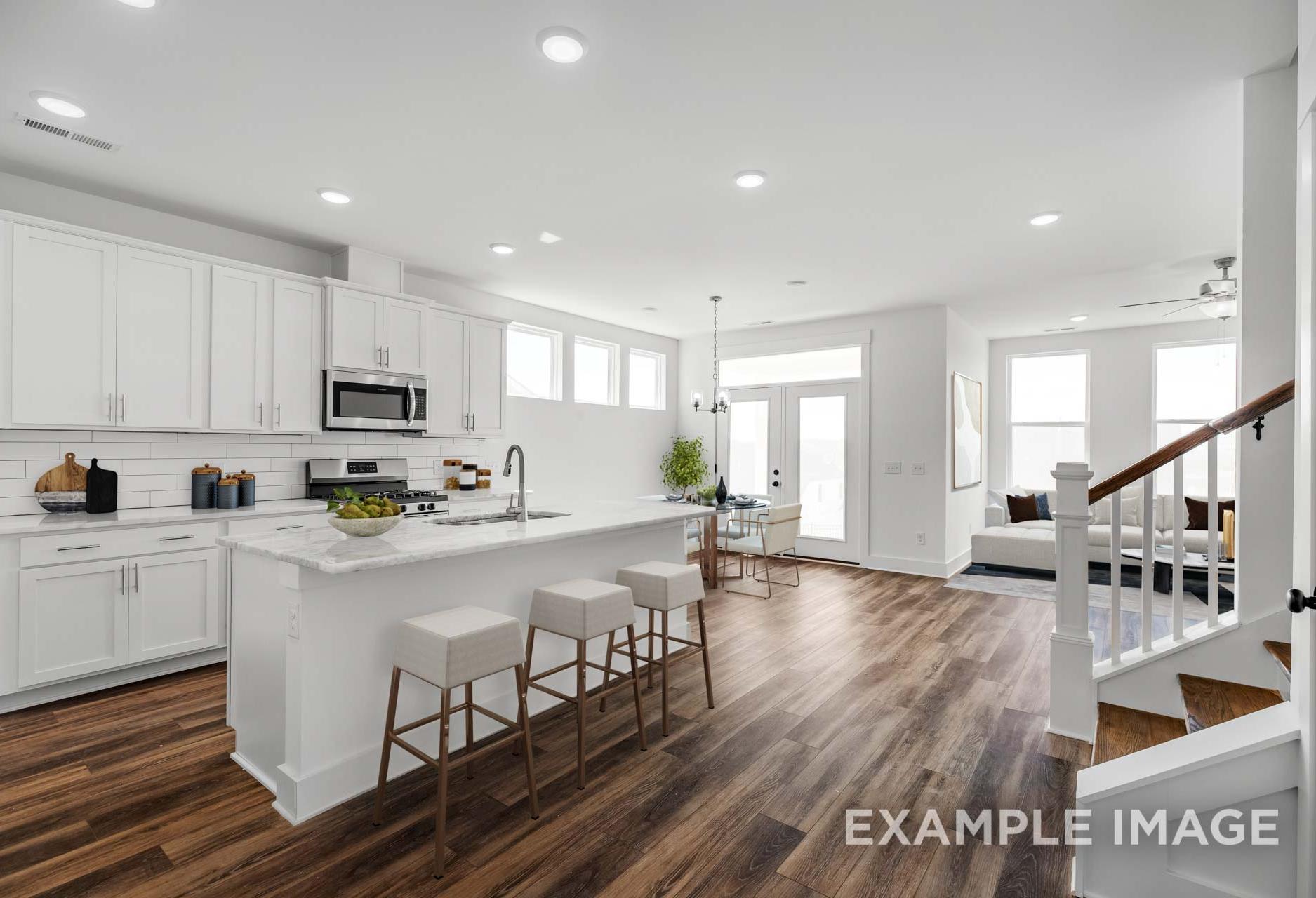 Spacious open-concept kitchen in The Ash M home with white shaker cabinets, large island, bar stools, and adjacent living area