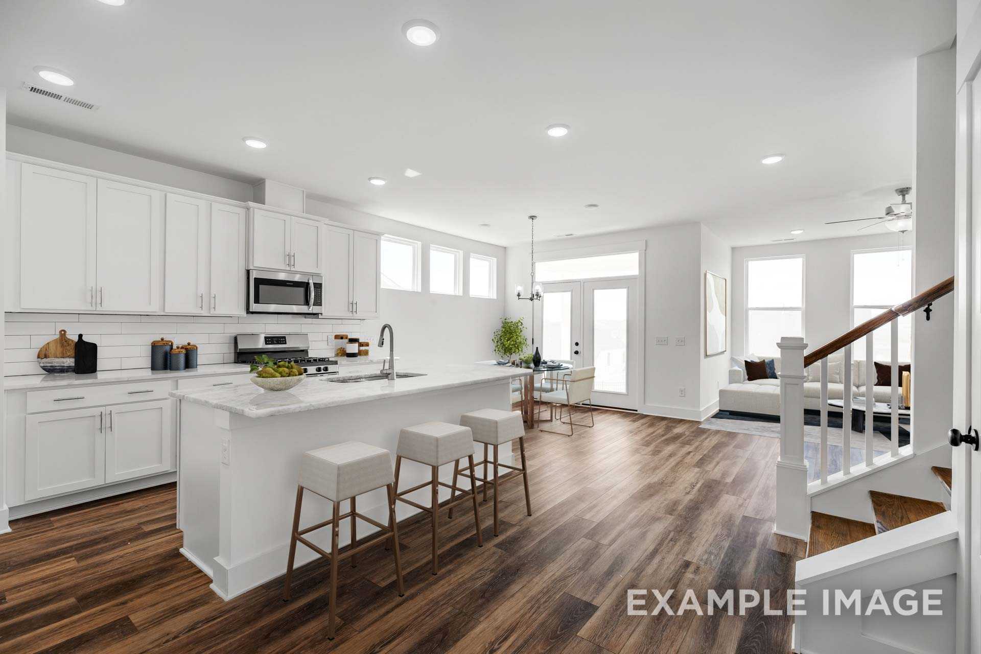 Open-concept kitchen in The Ash C floor plan with white shaker cabinets, large island, bar stools, and adjacent living area