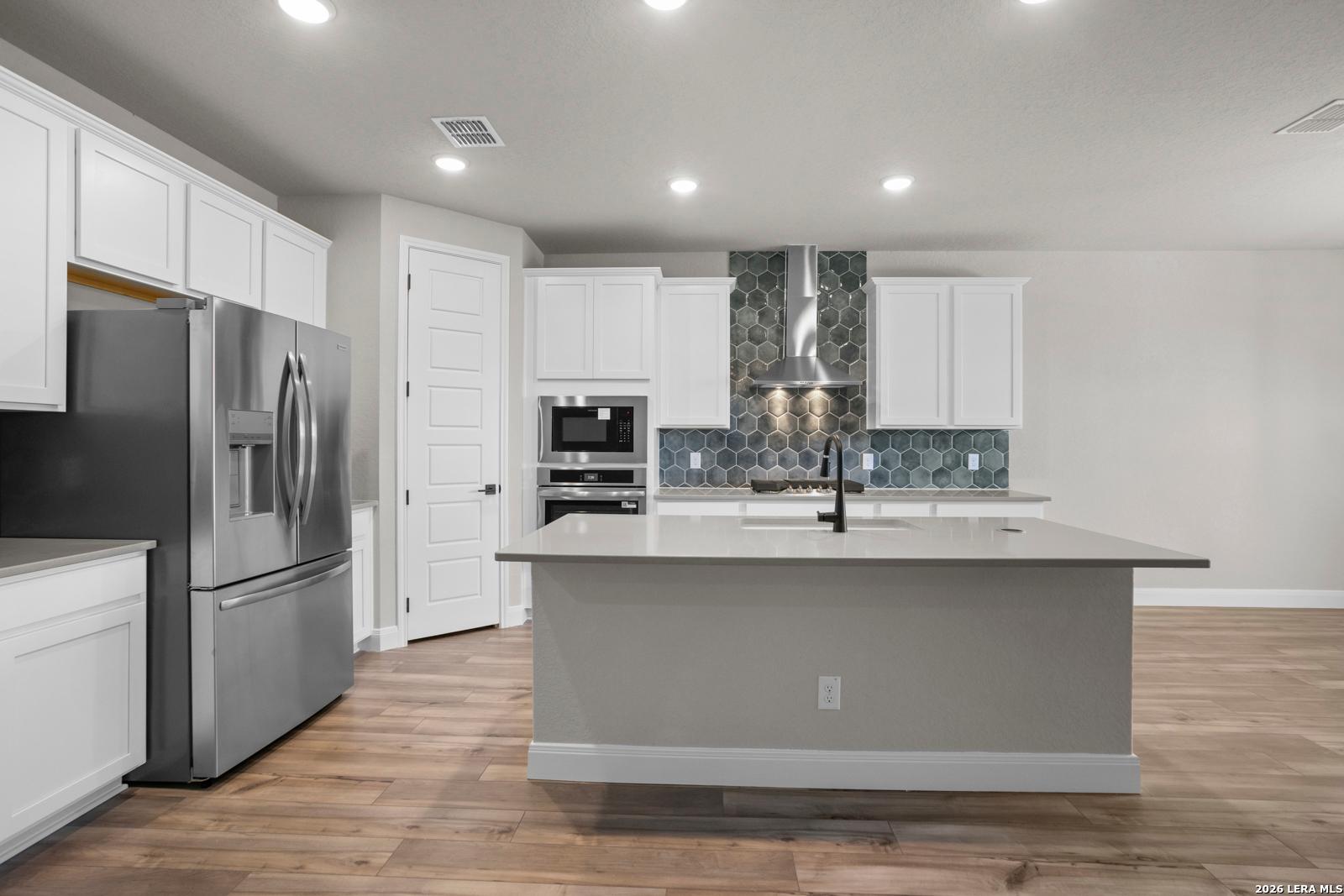 Modern kitchen with white cabinets, stainless appliances, and hexagon tile backsplash in The Jennings G floor plan, Ladera.
