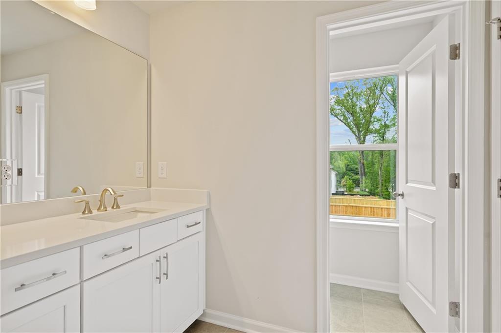 Bright bathroom vanity with single sink, large mirror, and open door to lush backyard in Davidson Homes The Cary B, Kennesaw, GA