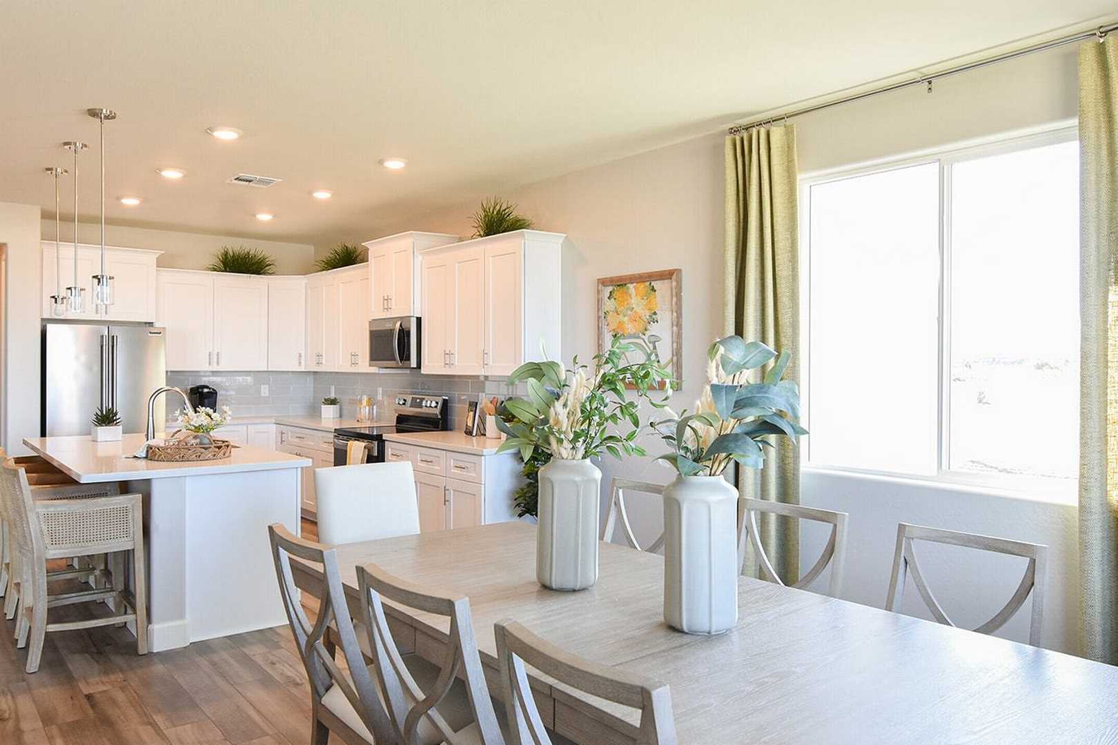 Spacious open-concept kitchen and dining in The Summit B with white cabinets, large island, pendant lights, and plants