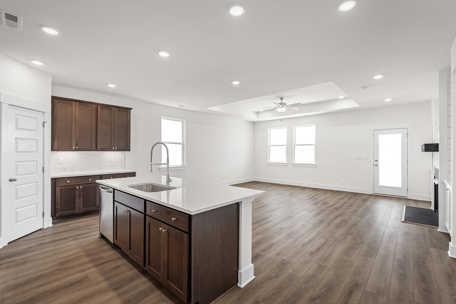 Open-concept kitchen with dark wood cabinets, white island, and luxury vinyl plank flooring in Davidson Homes Cottonwood E, Gallatin TN