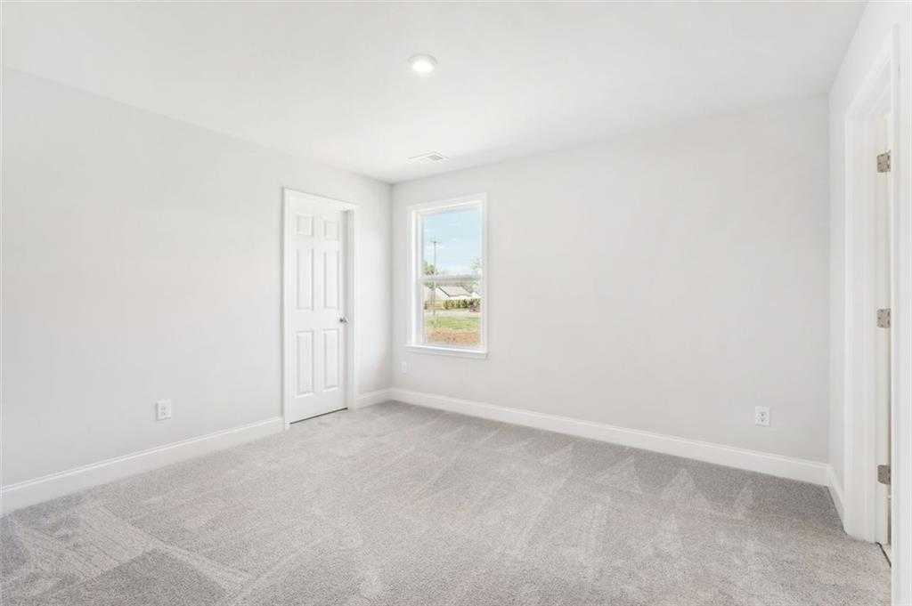 Bright secondary bedroom featuring gray carpet, light walls, and large window in Davidson Homes The Hickory C, Hoschton, GA