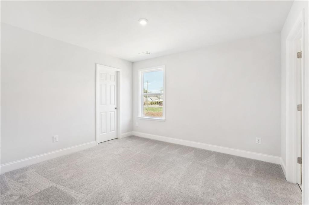 Bright secondary bedroom featuring gray carpet, light walls, and large window in Davidson Homes The Hickory C, Hoschton, GA