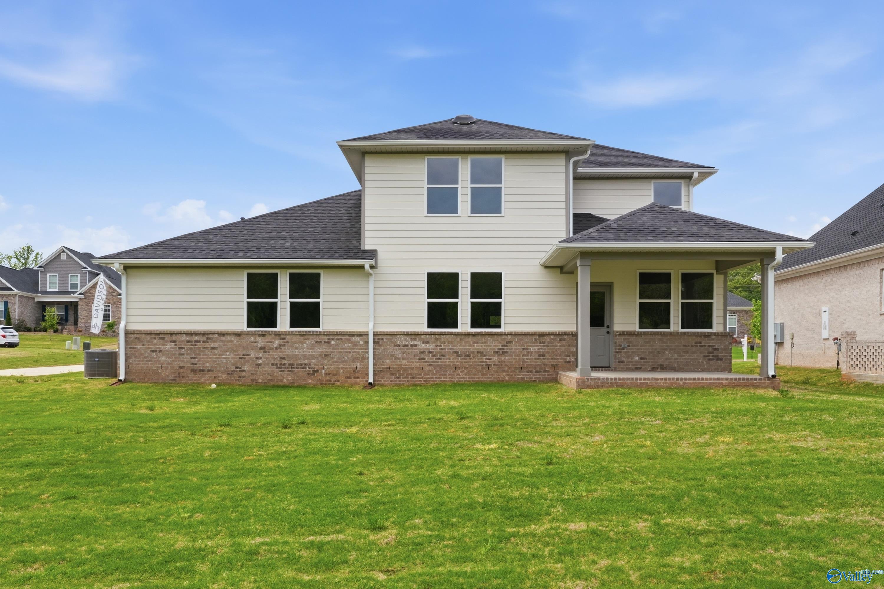 Two-story beige home with brick base, dark shingle roof, and covered porch in Riverton Preserve, Huntsville, Alabama