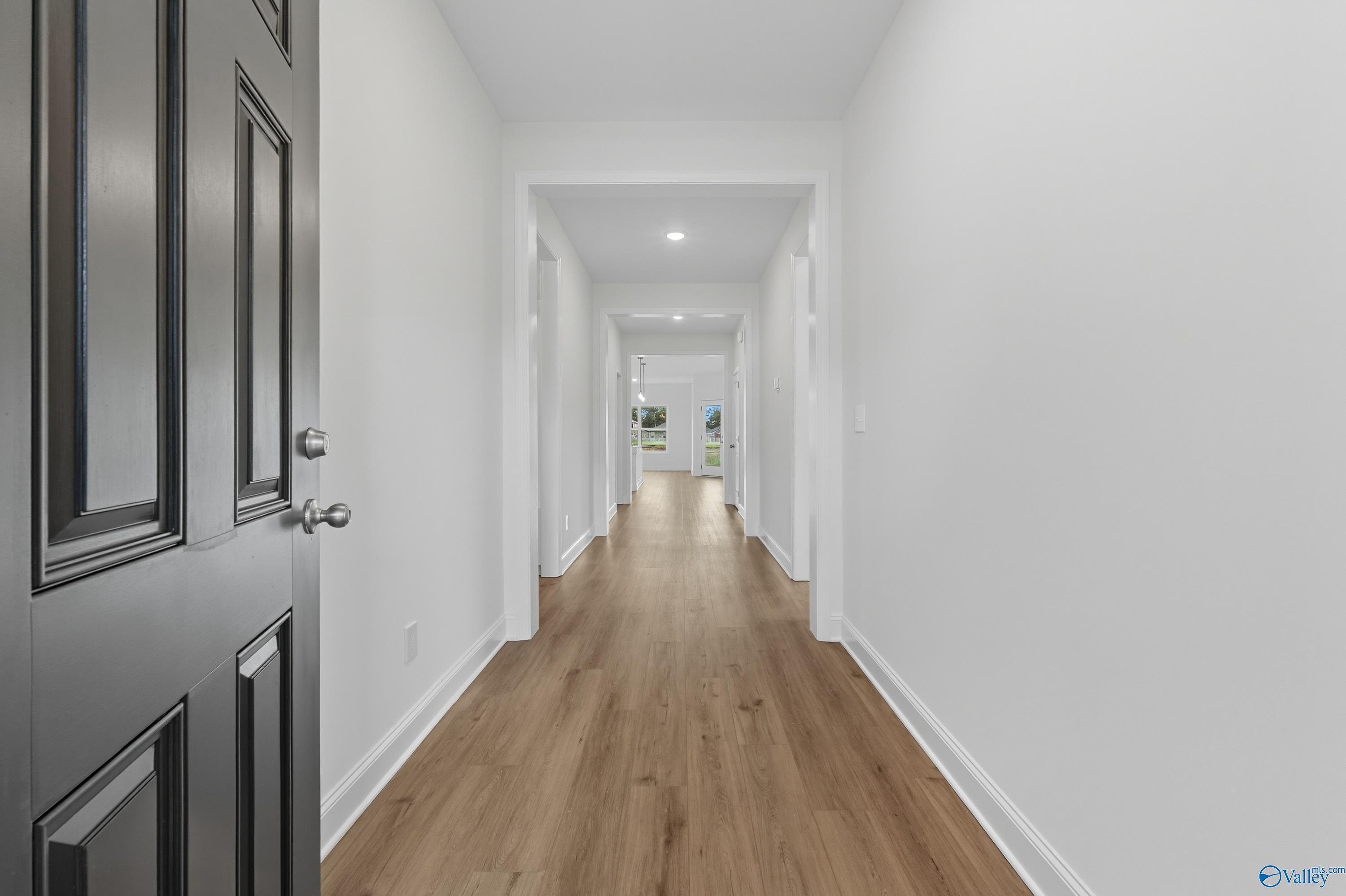 Bright entry hallway with open dark front door, hardwood floors, and white walls in Davidson Homes The Everett, Meridianville AL