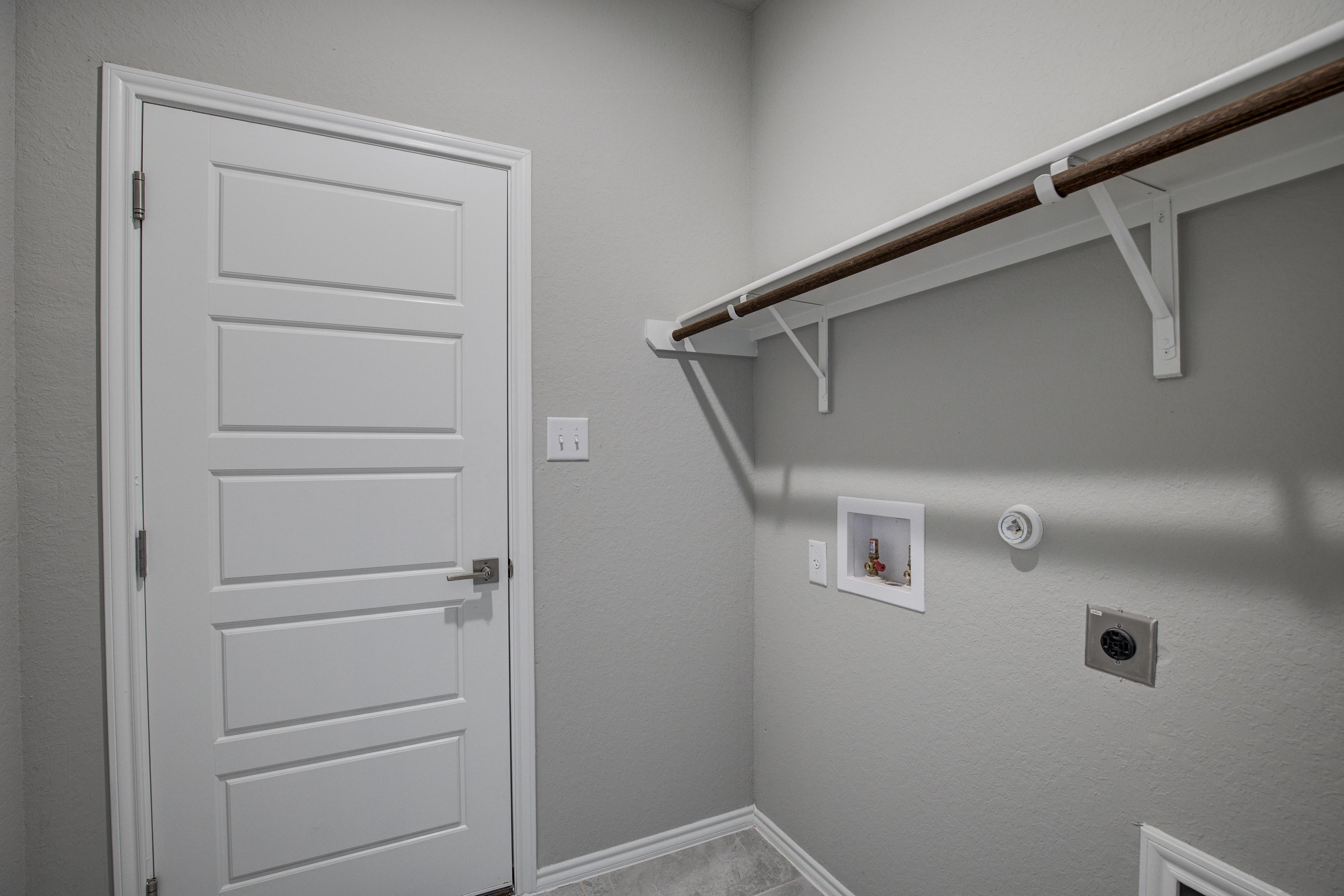 The Frio D laundry room with gray walls, wooden open shelving, stackable washer-dryer space and utility hookups
