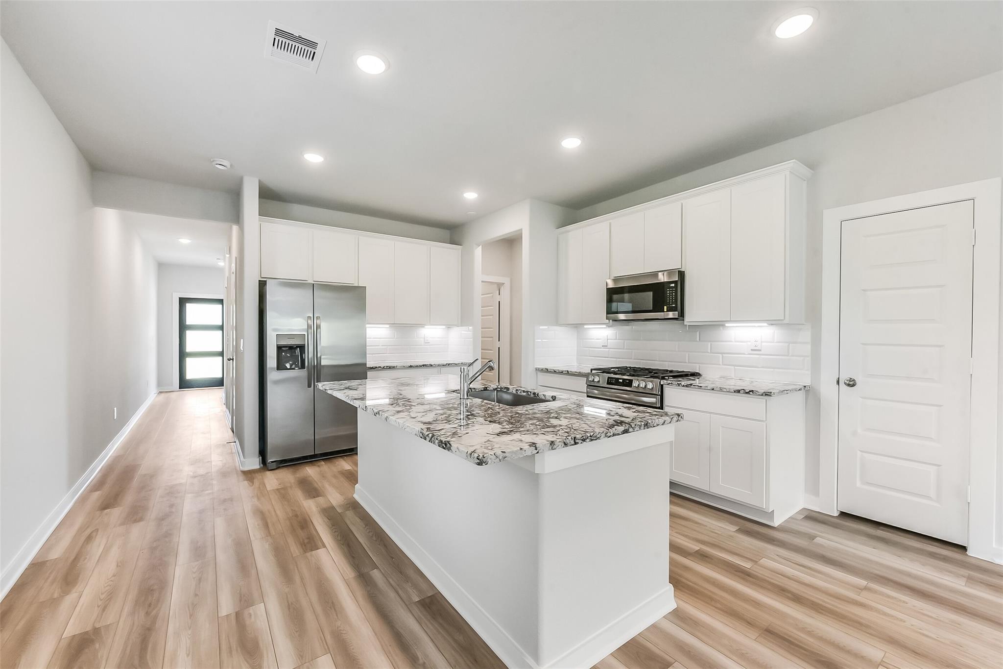 Modern white kitchen with granite island, stainless steel appliances, subway tile backsplash in The Frio G, Magnolia Texas