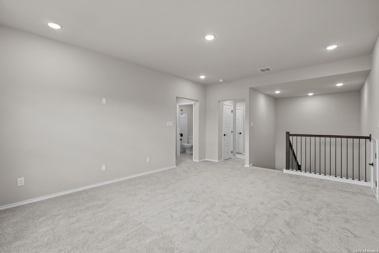 Spacious carpeted game room loft with wrought iron stair railing and recessed lighting in Davidson Homes Sequoia C, San Antonio
