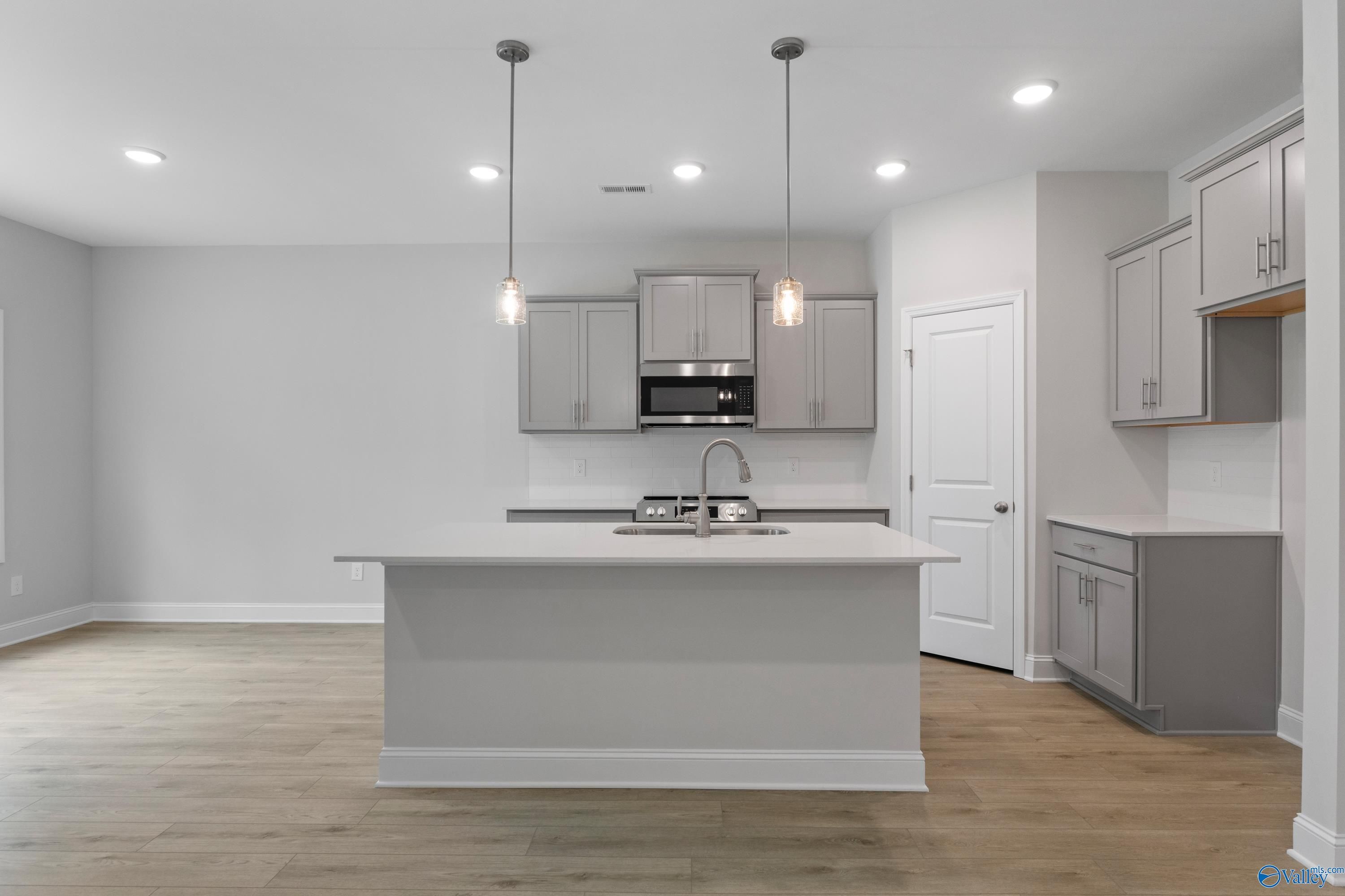 Modern white kitchen island with stainless steel appliances and pendant lights in The Asheville floor plan, Huntsville AL