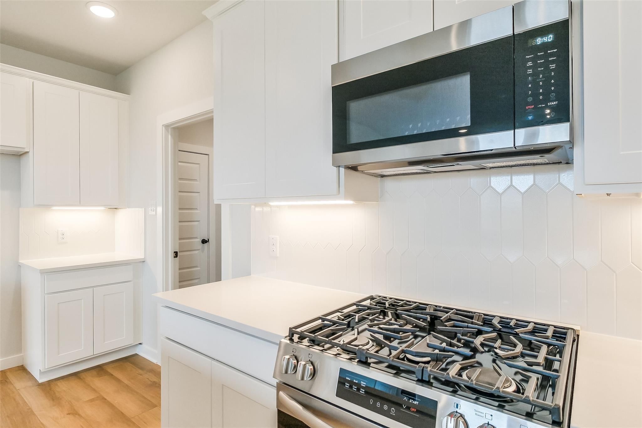 Modern white kitchen featuring stainless steel microwave, gas cooktop, and hexagonal tile backsplash in Davidson Homes The Tierra B, Beasley, Texas